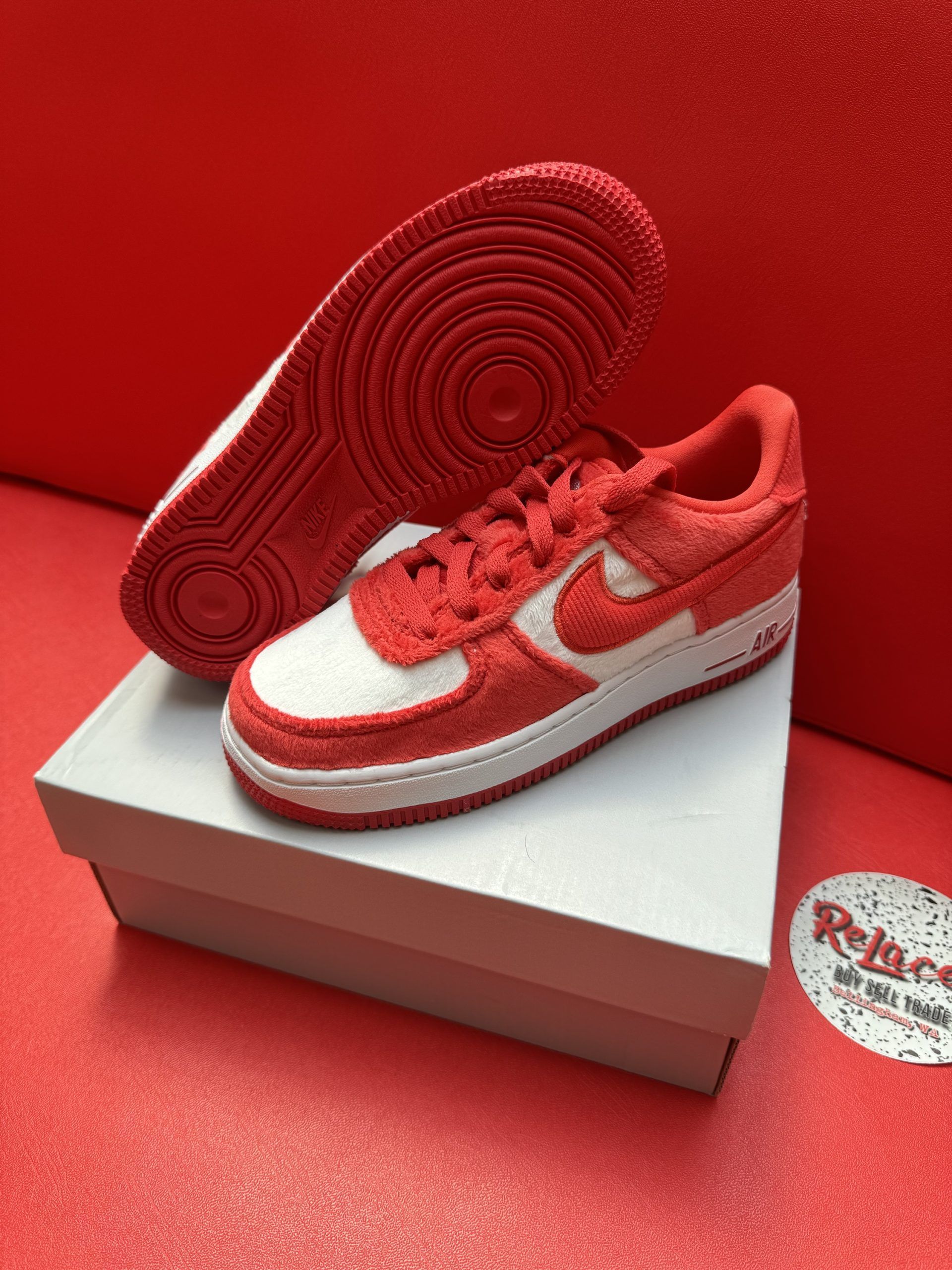 Red and white Nike Air Force 1 sneakers on a white box, red sole visible.