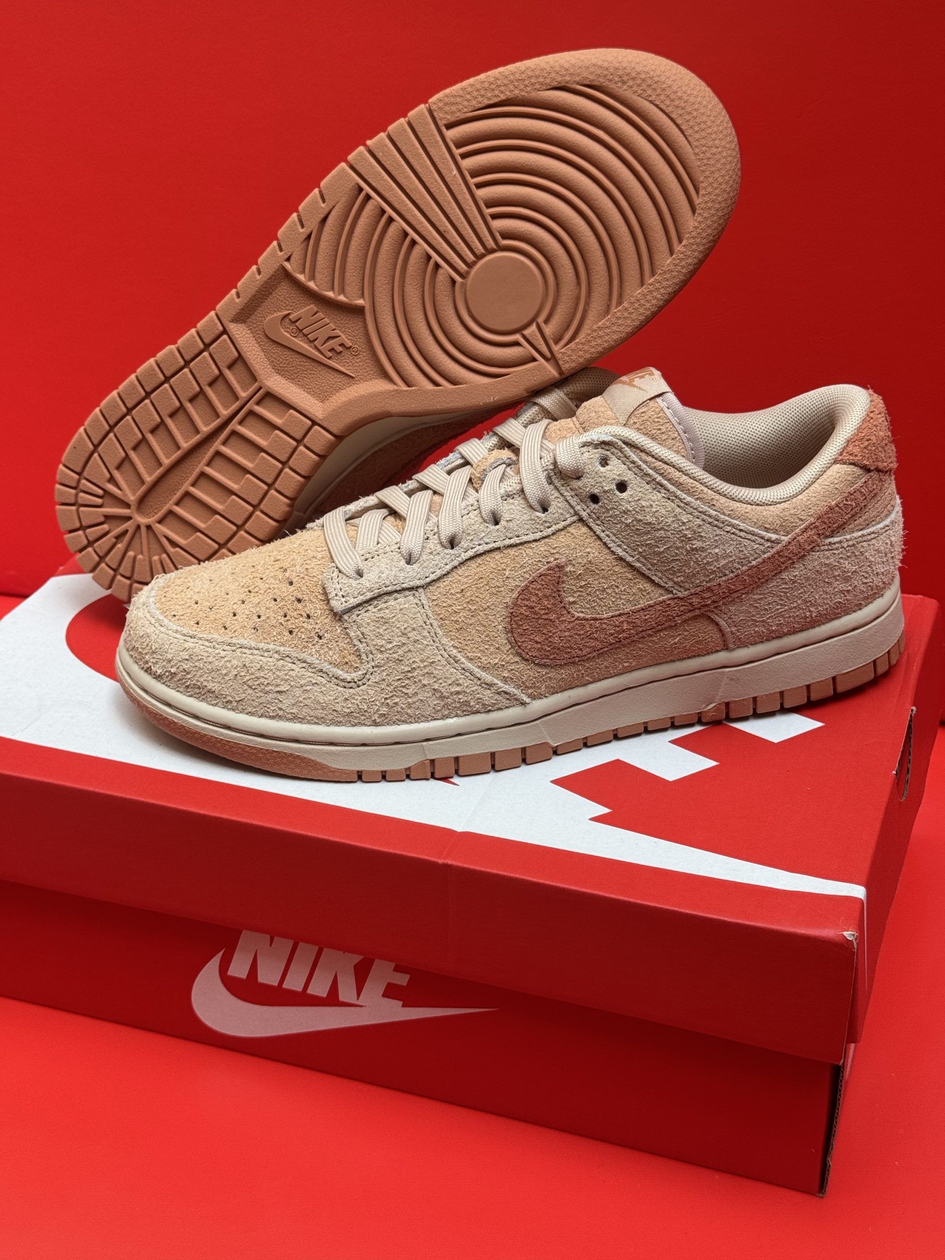 Nike Dunk Low sneakers with brown textured uppers and soles, on top of a red Nike box, against a red background.