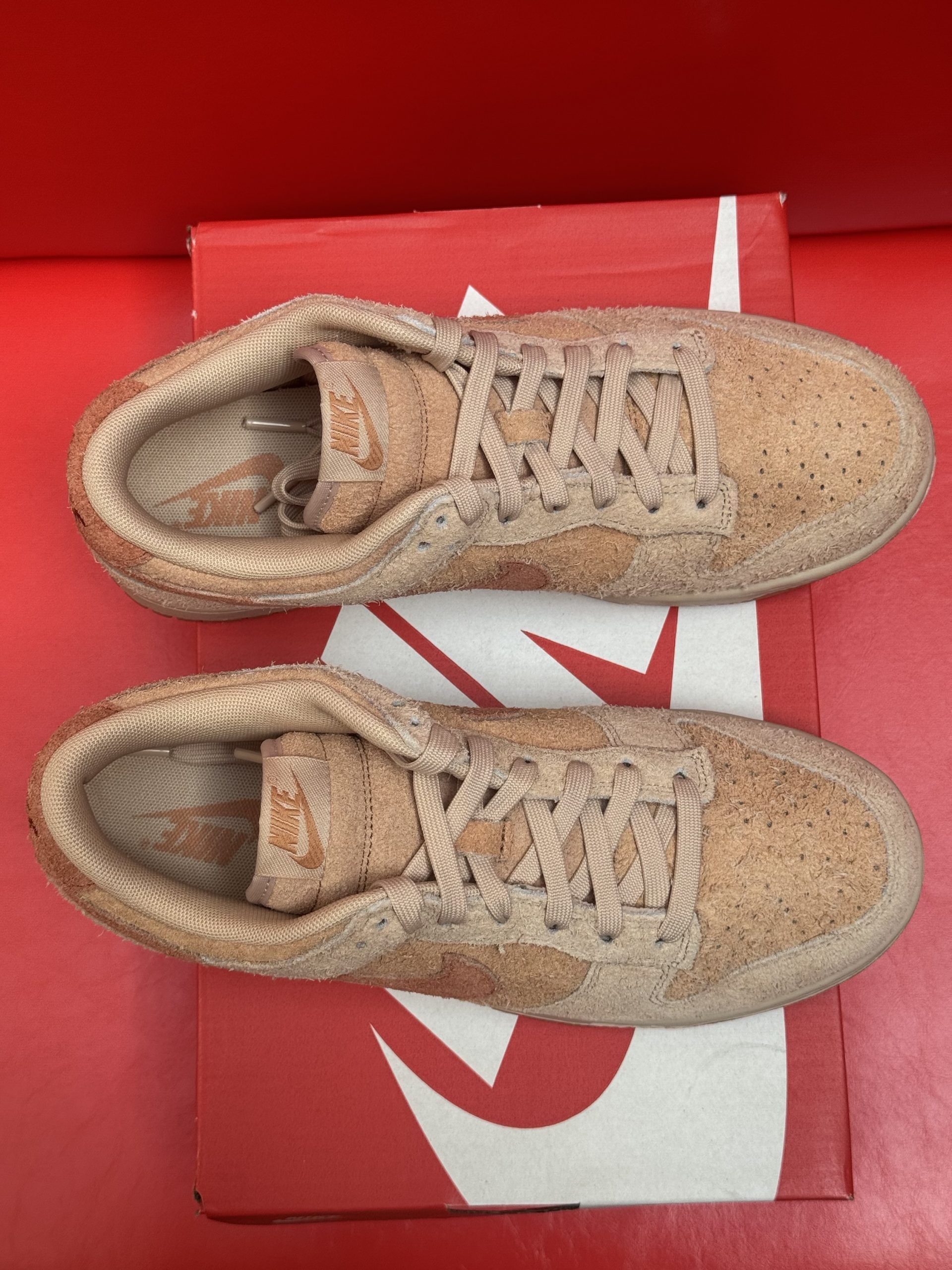 Nike Dunk Low sneakers with brown textured uppers and soles, on top of a red Nike box, against a red background.