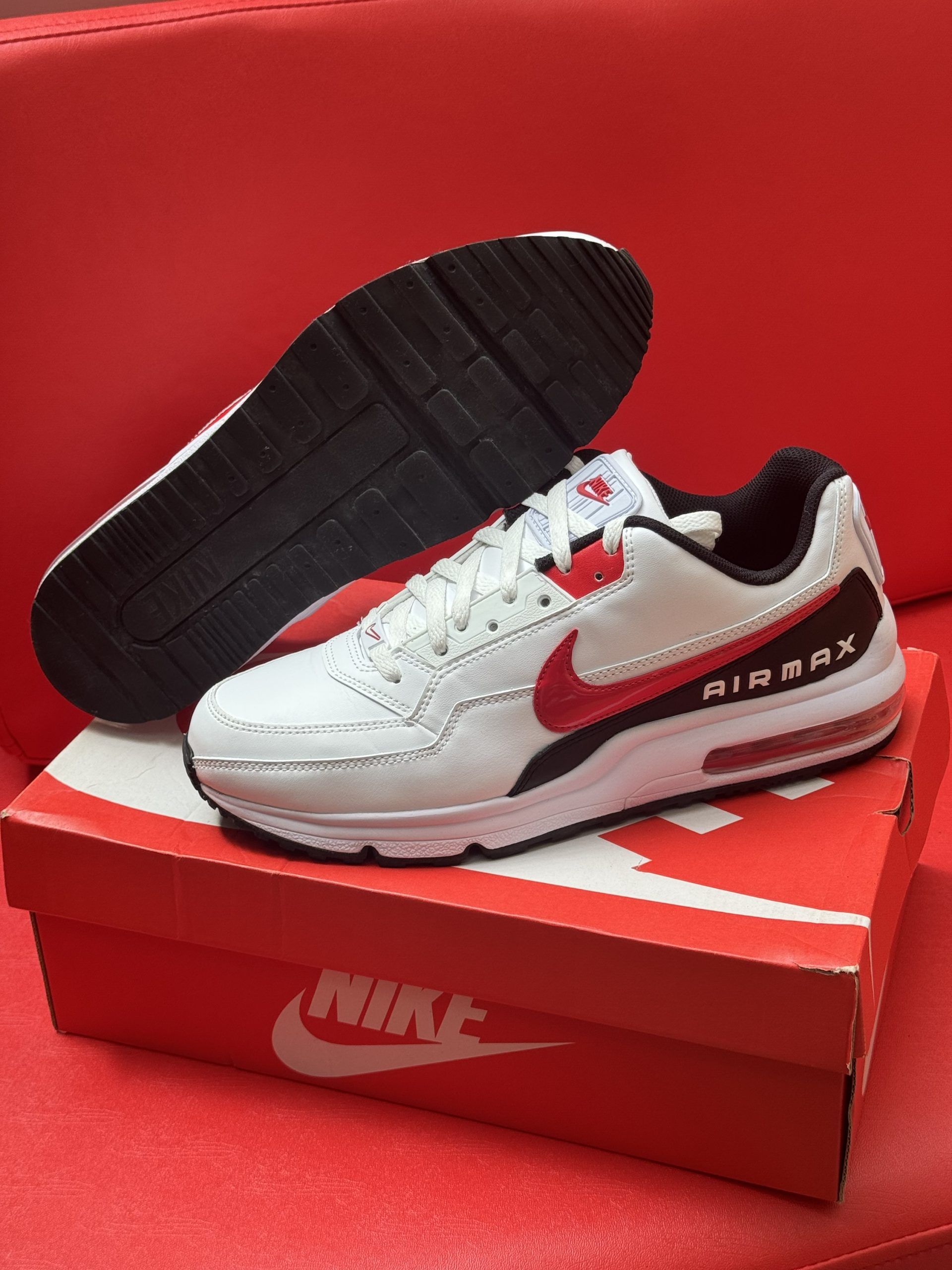 White Nike Air Max sneakers with red accents, on a red shoebox, on a red surface.