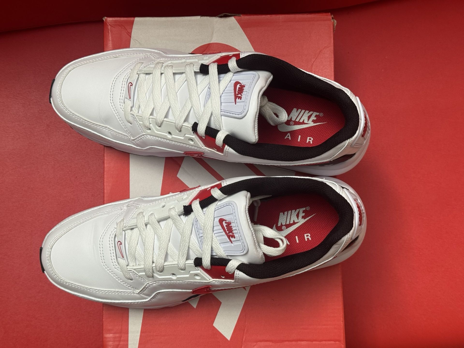 White Nike Air Max sneakers with red accents, on a red shoebox, on a red surface.