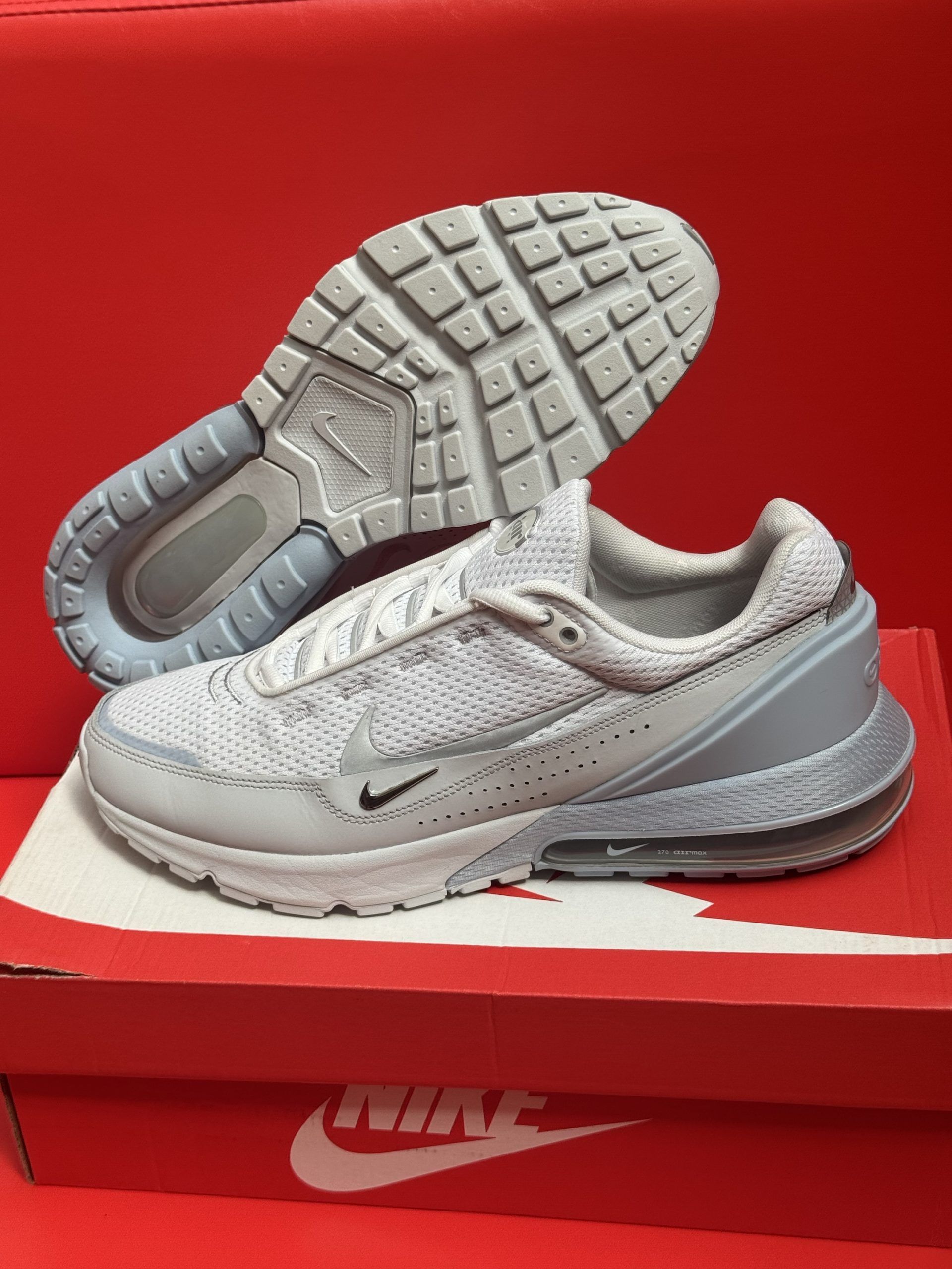 Light gray Nike sneakers on a red Nike box with a gray sole and a red background.