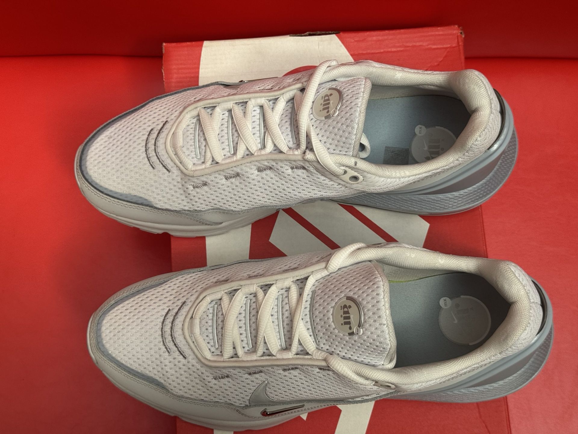 Light gray Nike sneakers on a red Nike box with a gray sole and a red background.