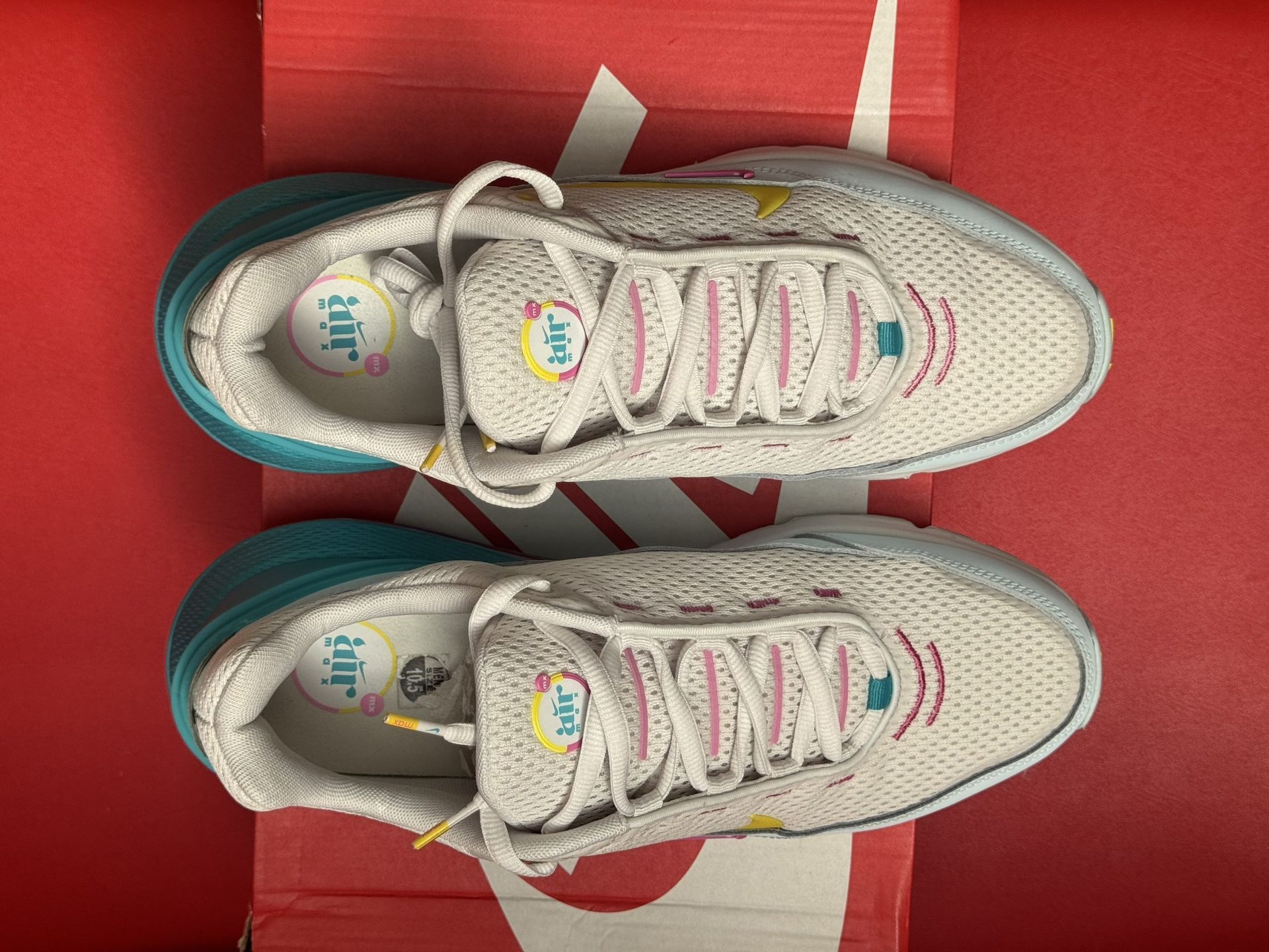 White and blue Nike Air Max shoes with yellow and pink accents, set on a Nike box against a red backdrop.
