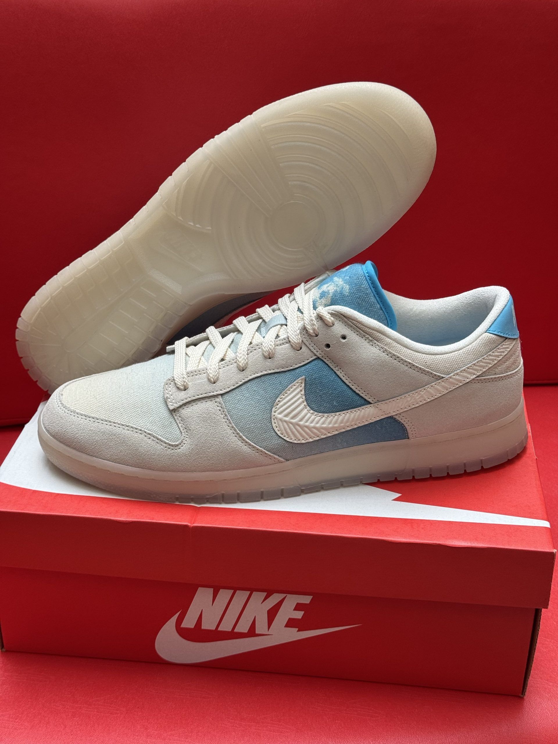 Nike Dunk Low sneakers in white and blue, sitting on red box, sole visible.