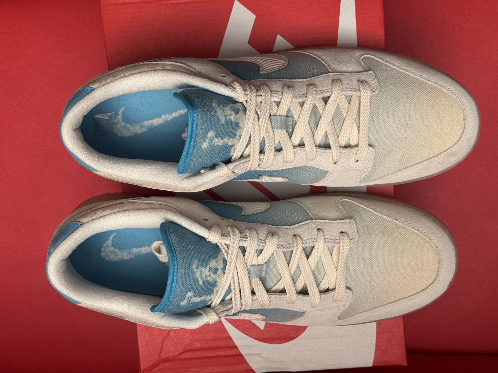 Nike Dunk Low sneakers in white and blue, sitting on red box, sole visible.