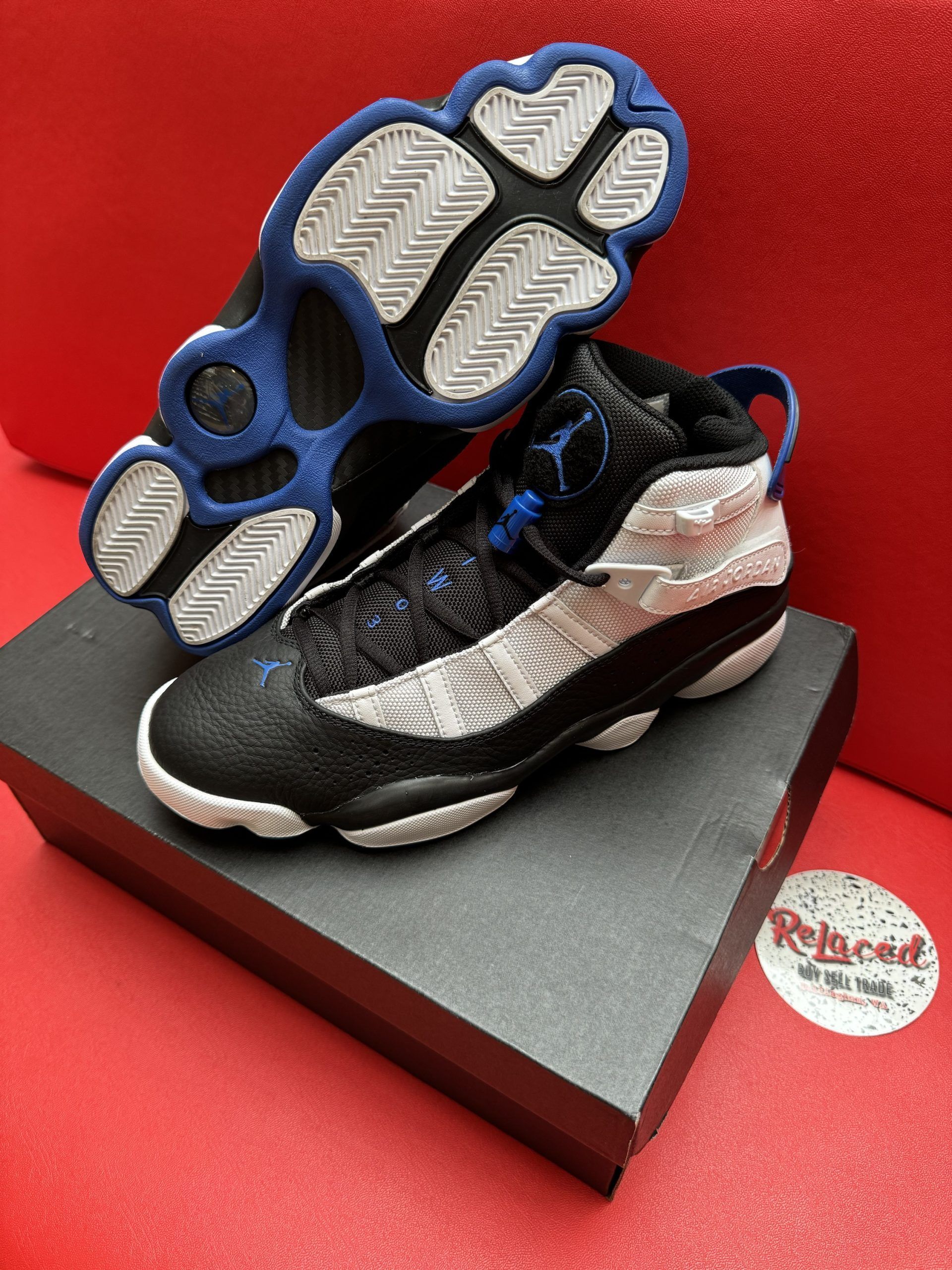 Air Jordan 6 Rings sneakers in black, white, and blue, displayed on a black box, with the sole visible.