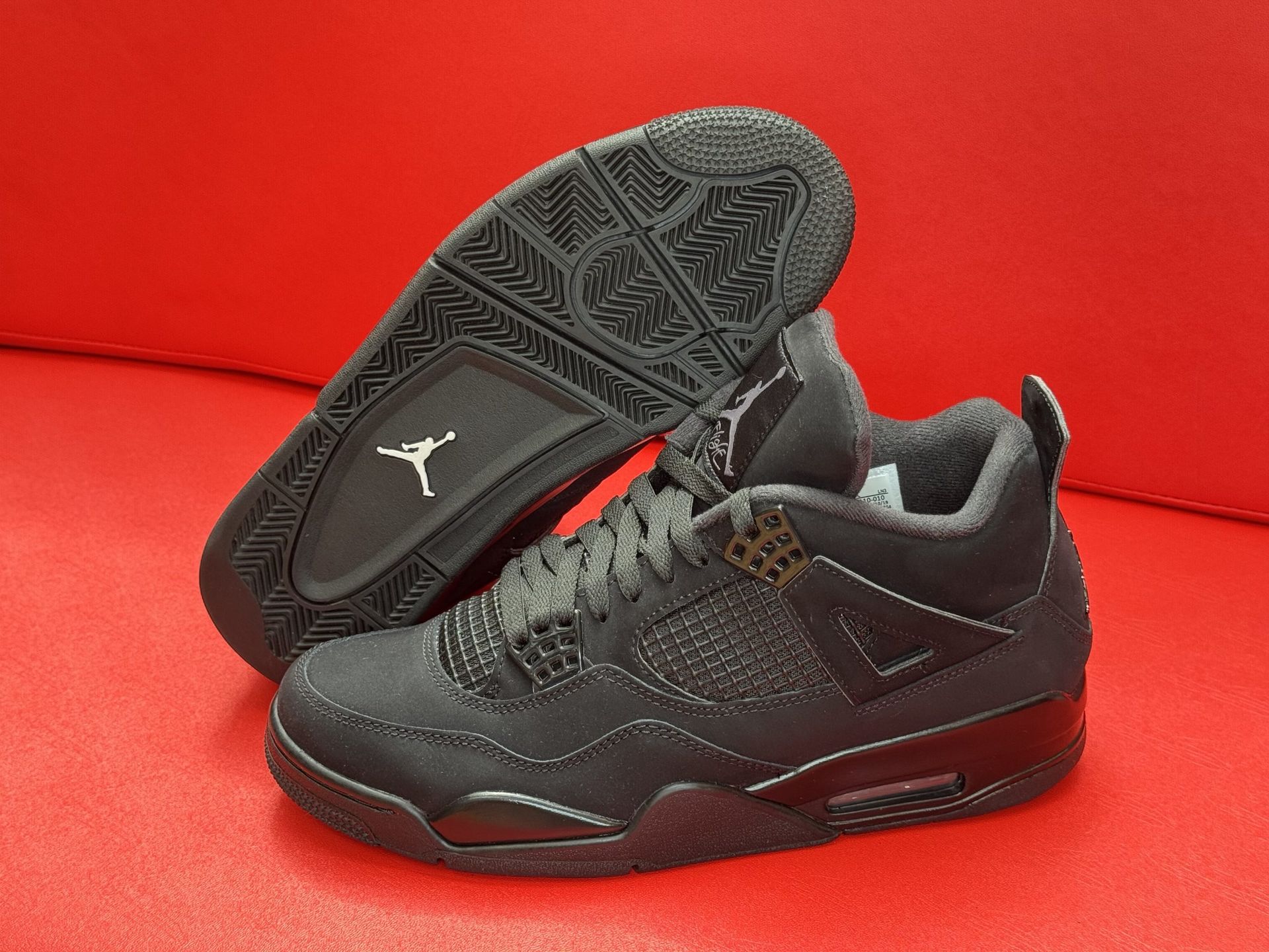 Black Air Jordan 4 sneakers on a red surface, with the sole visible.
