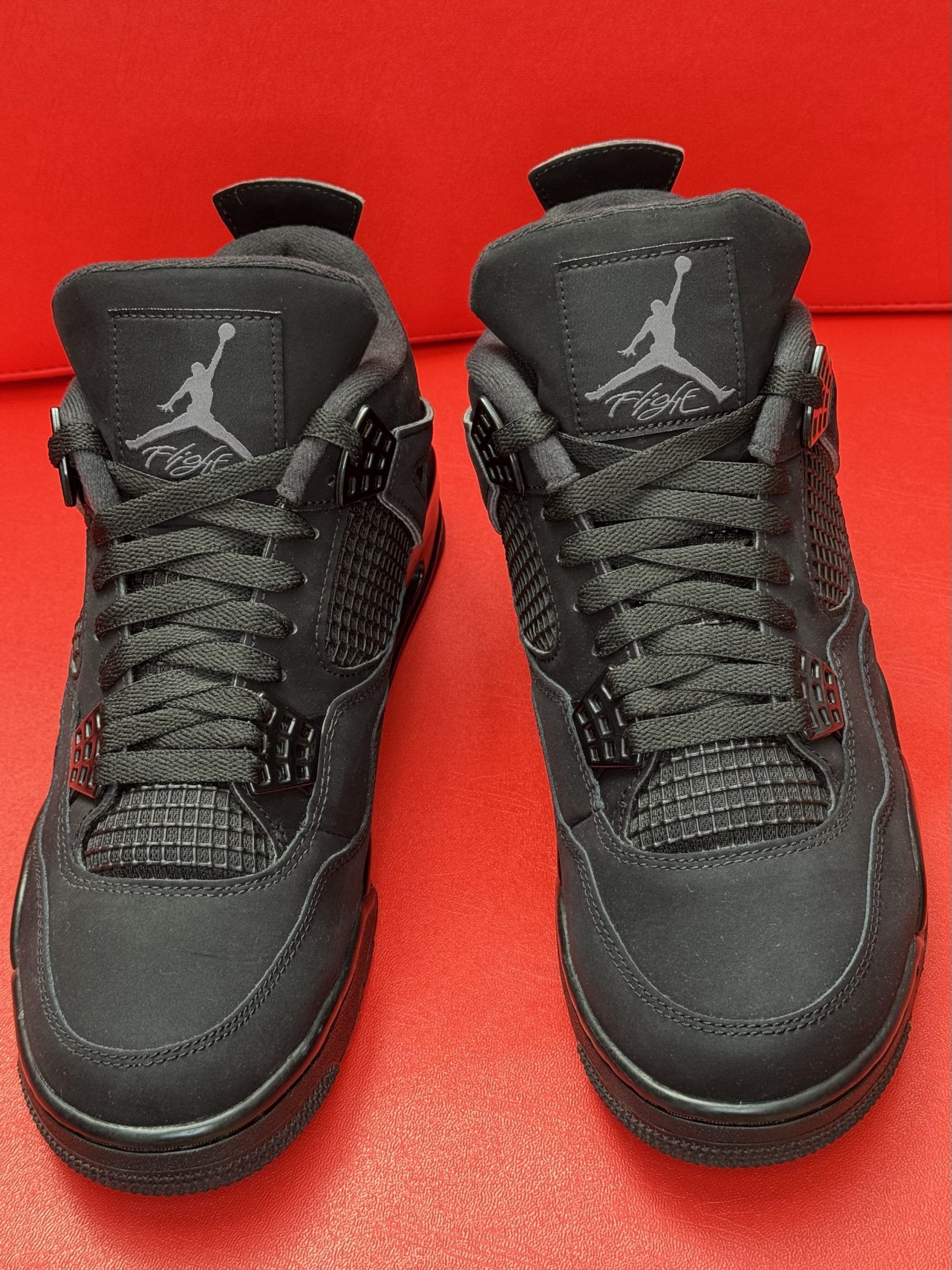 Black Air Jordan 4 sneakers on a red surface, with the sole visible.