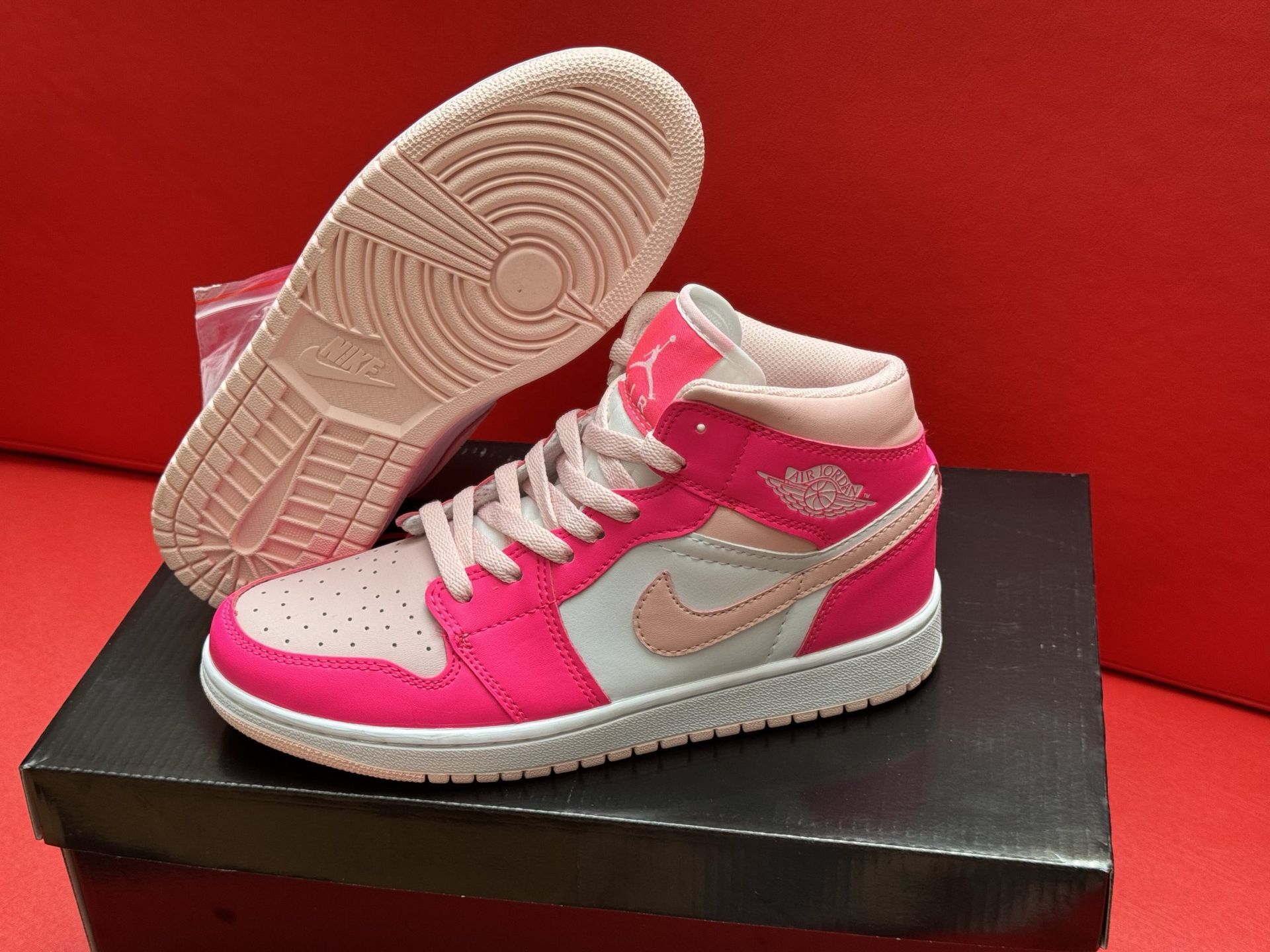 Pink and white Air Jordan sneakers on a black box, with a red background. The sole is visible.