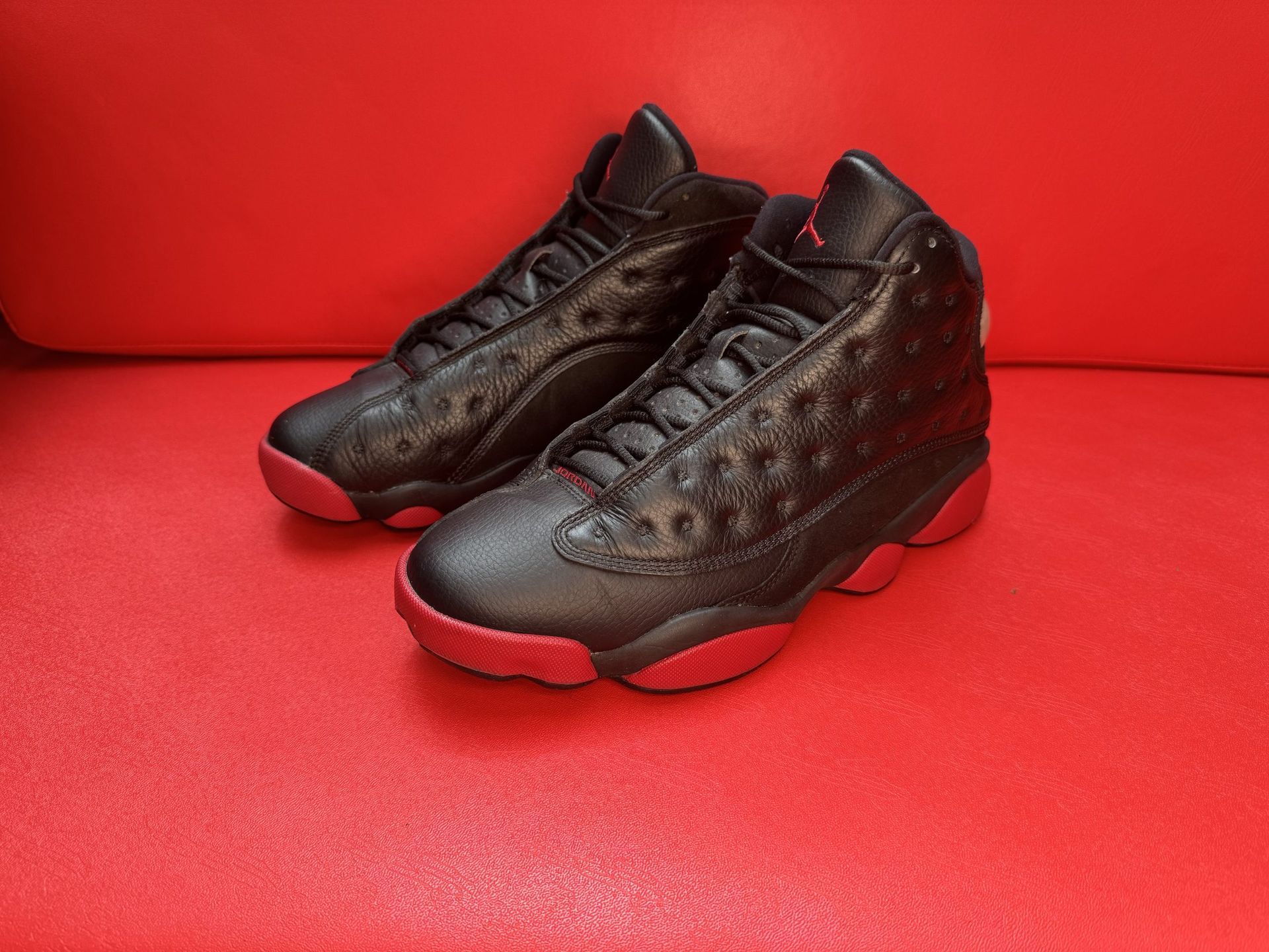 Black and red Air Jordan 13 sneakers on a red surface.