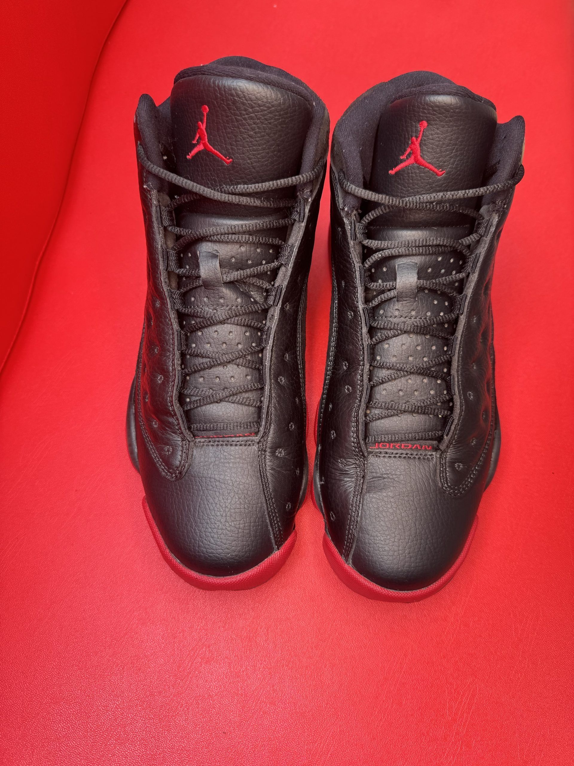 Black and red Air Jordan 13 sneakers on a red surface.