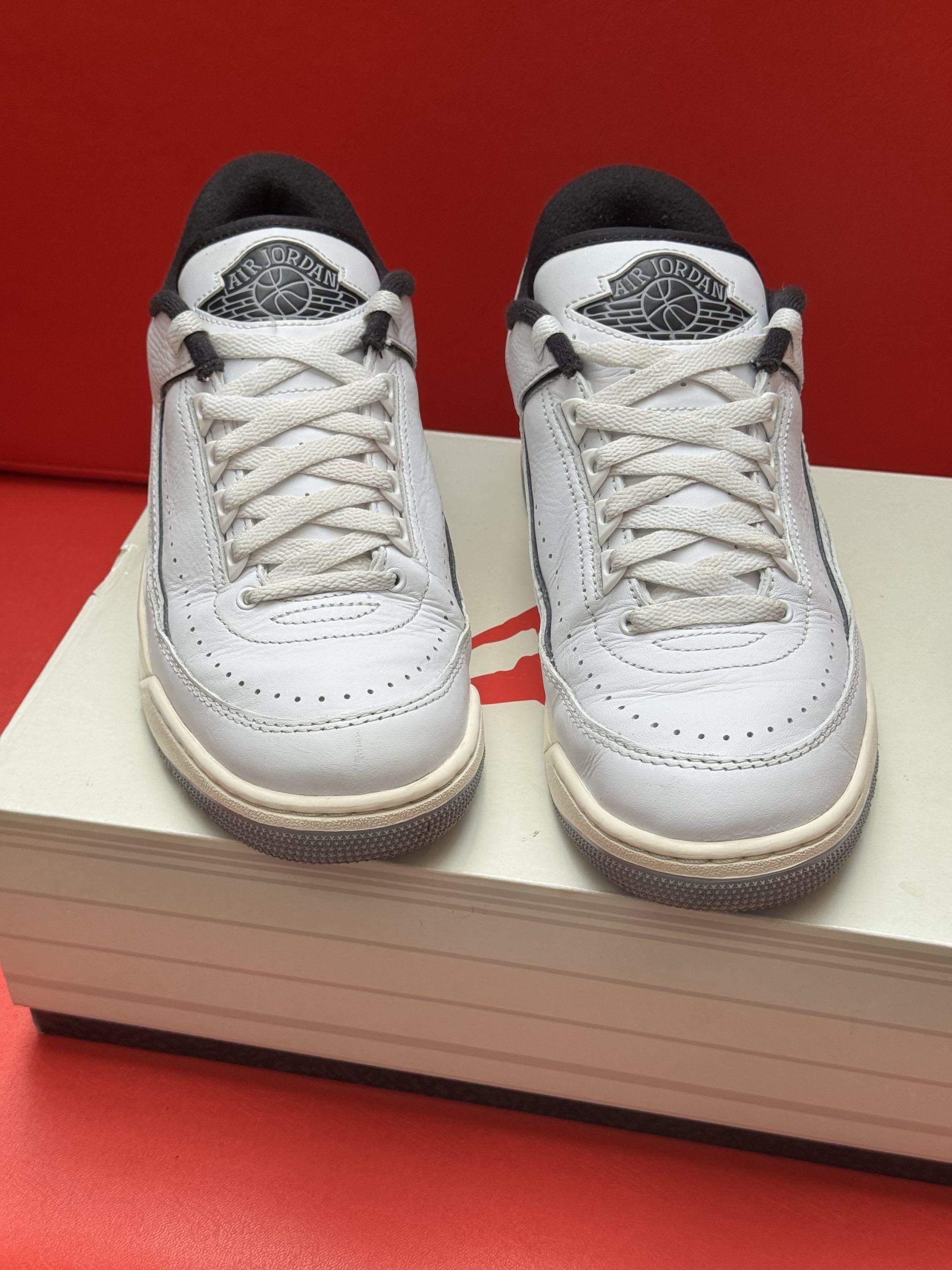 Pair of white and black Air Jordan 2 sneakers on a box, red background.