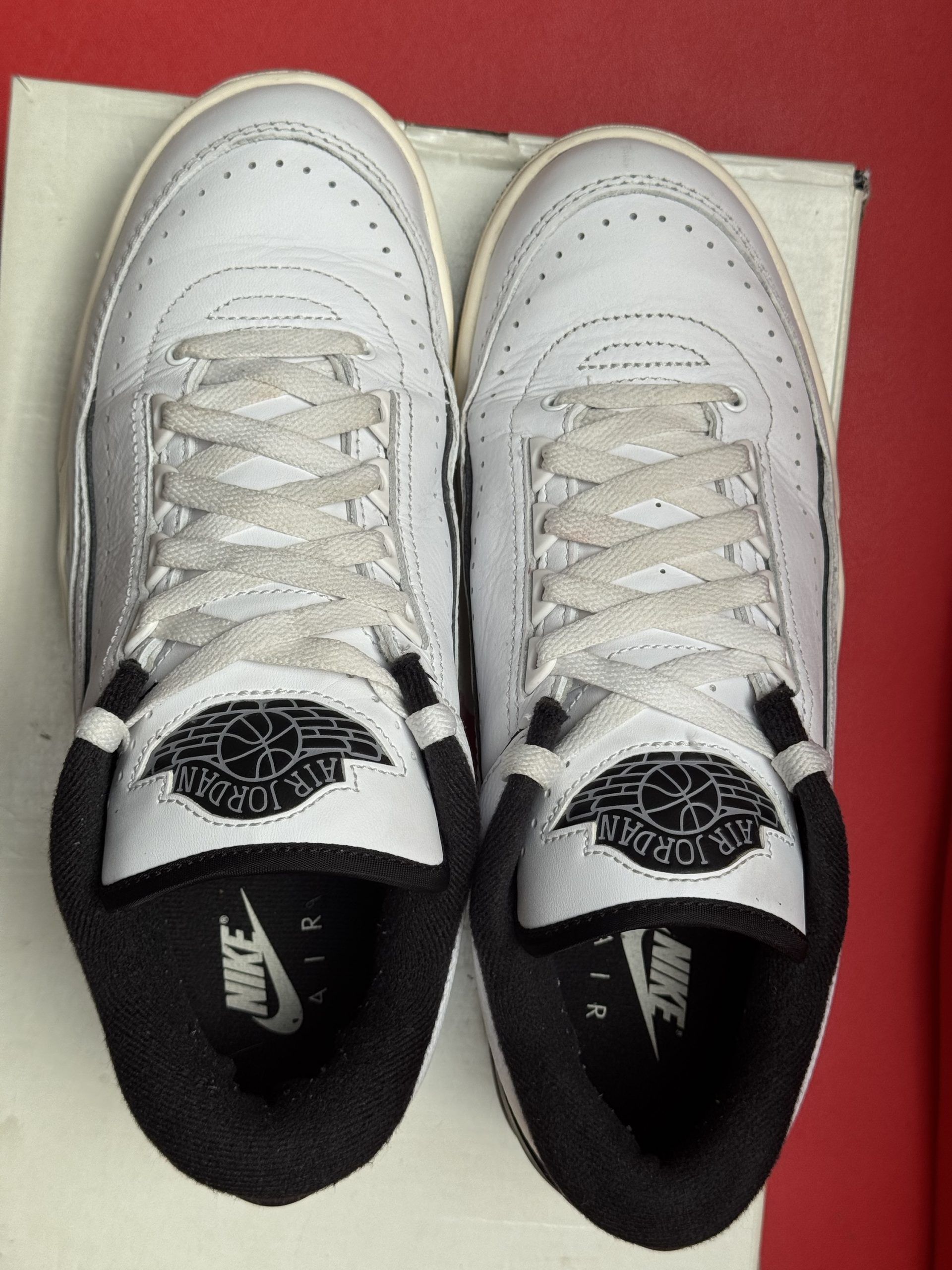 Pair of white and black Air Jordan 2 sneakers on a box, red background.