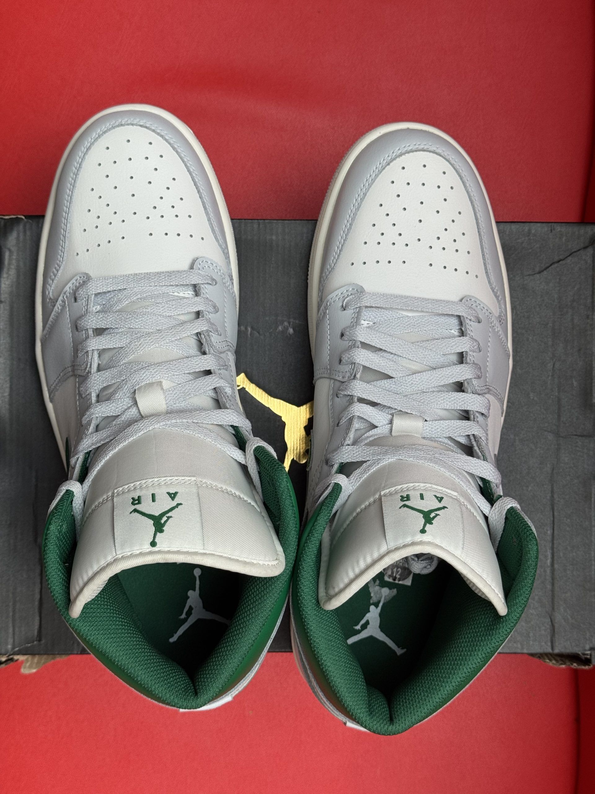 White and green Air Jordan 1 sneaker on black box, red background. Sole up.