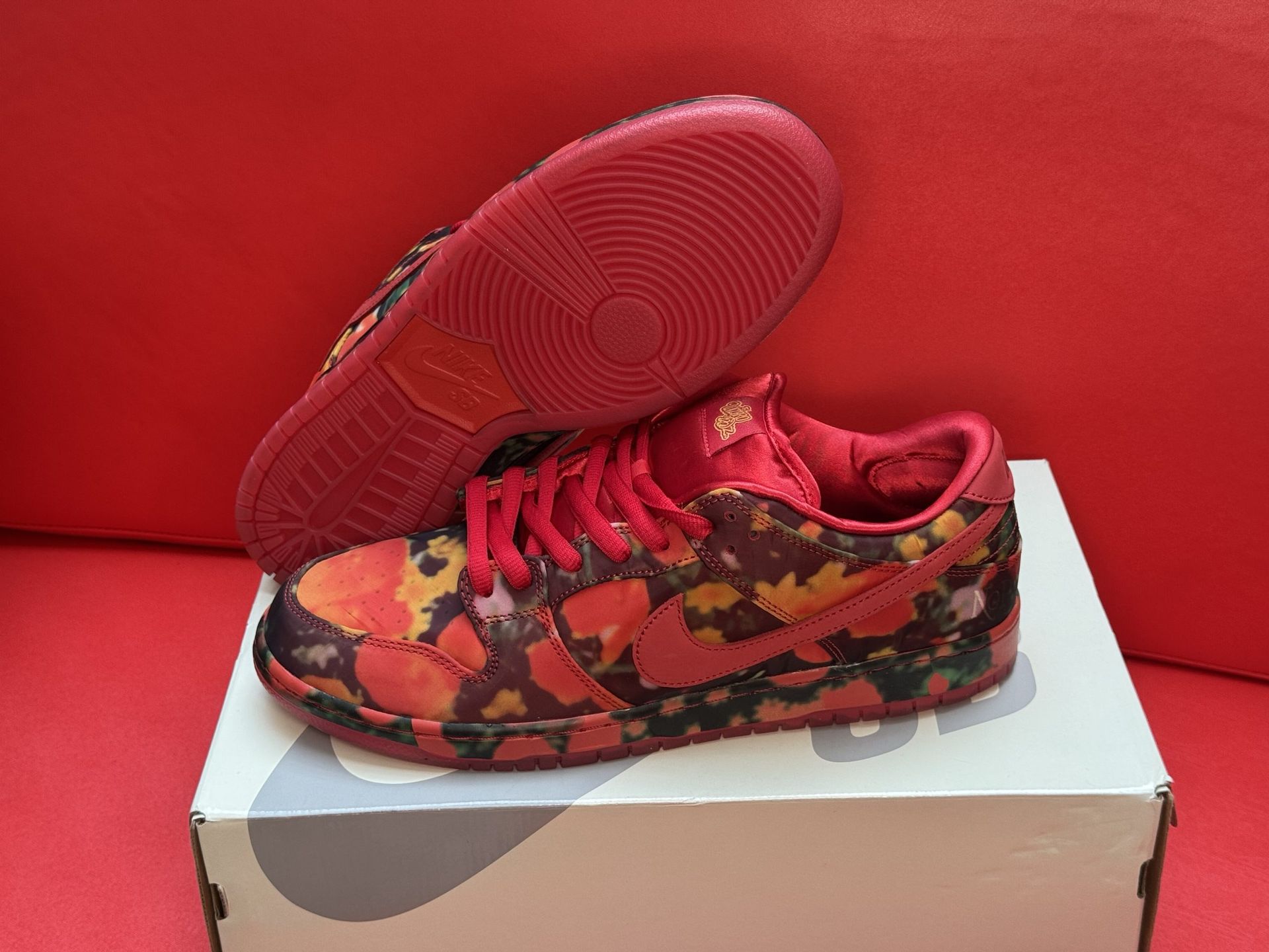 Red and floral patterned Nike Dunk Low sneakers on a white box, red background.
