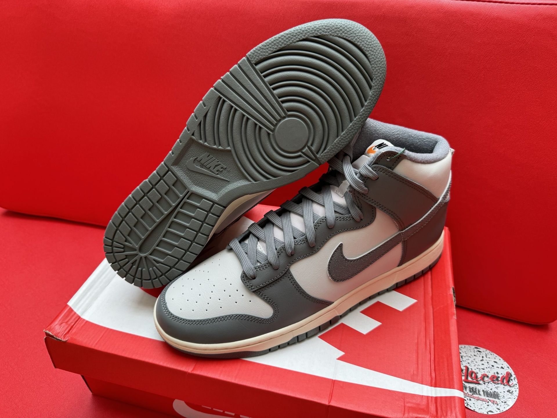 Nike Dunk High sneakers, gray and light gray, on a red box, red backdrop.