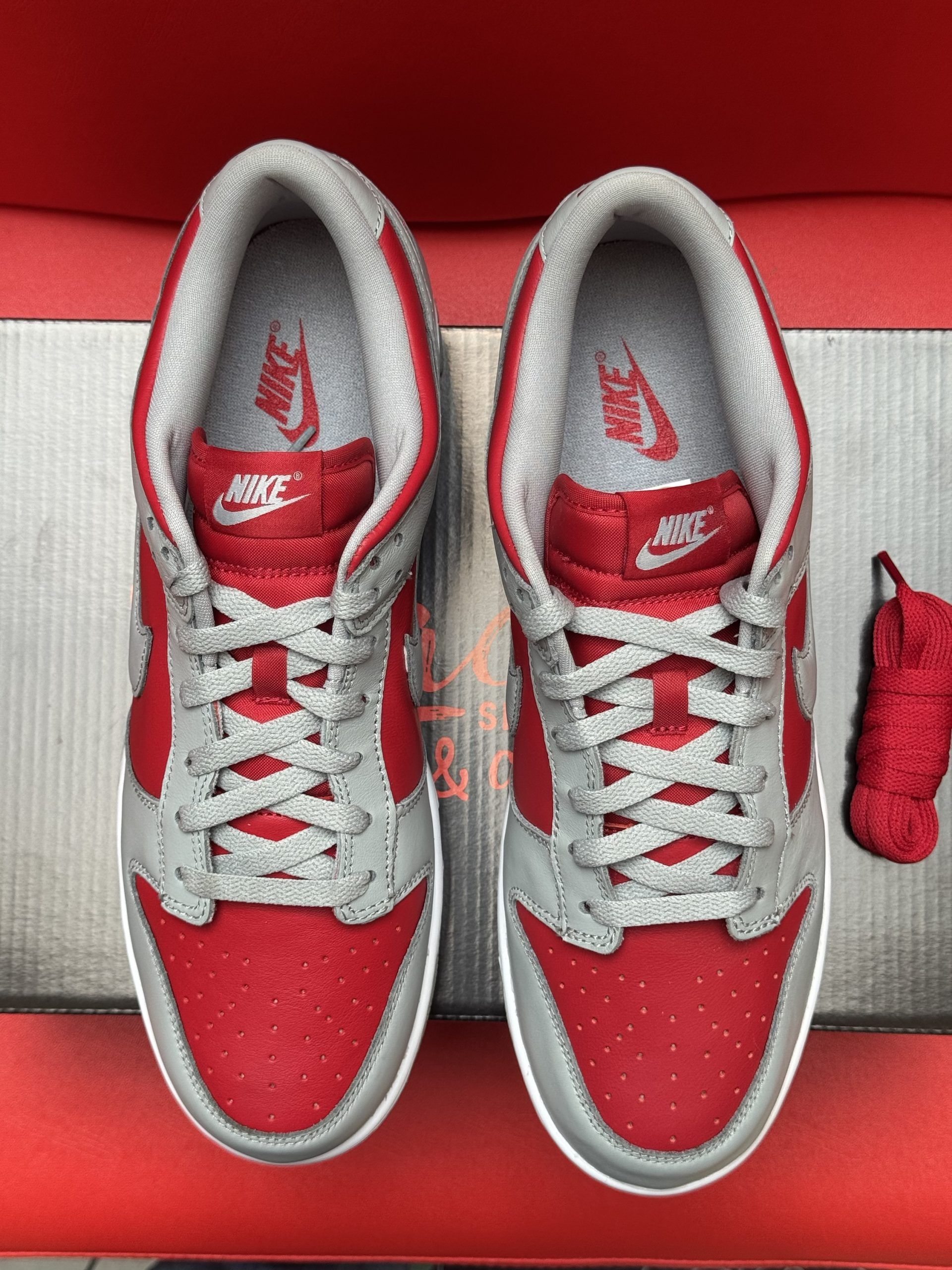 Nike Dunk Low sneakers, red and gray, with gray sole. One shoe rests on its side, the other inverted. Red background.