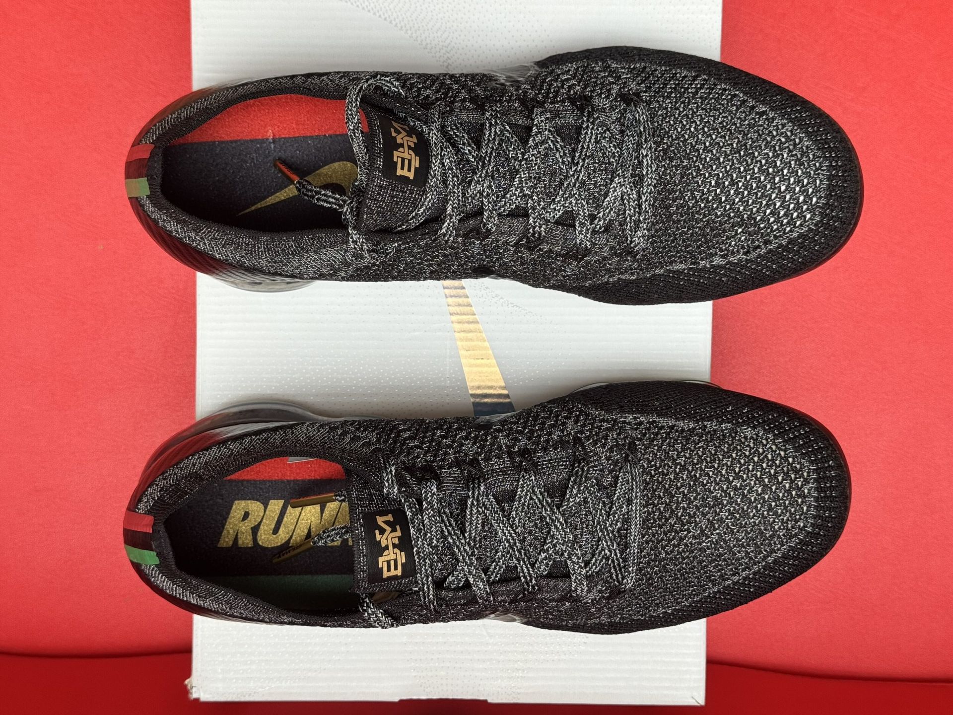 Black and gray Nike Air VaporMax Flyknit sneakers on a white box, red background.