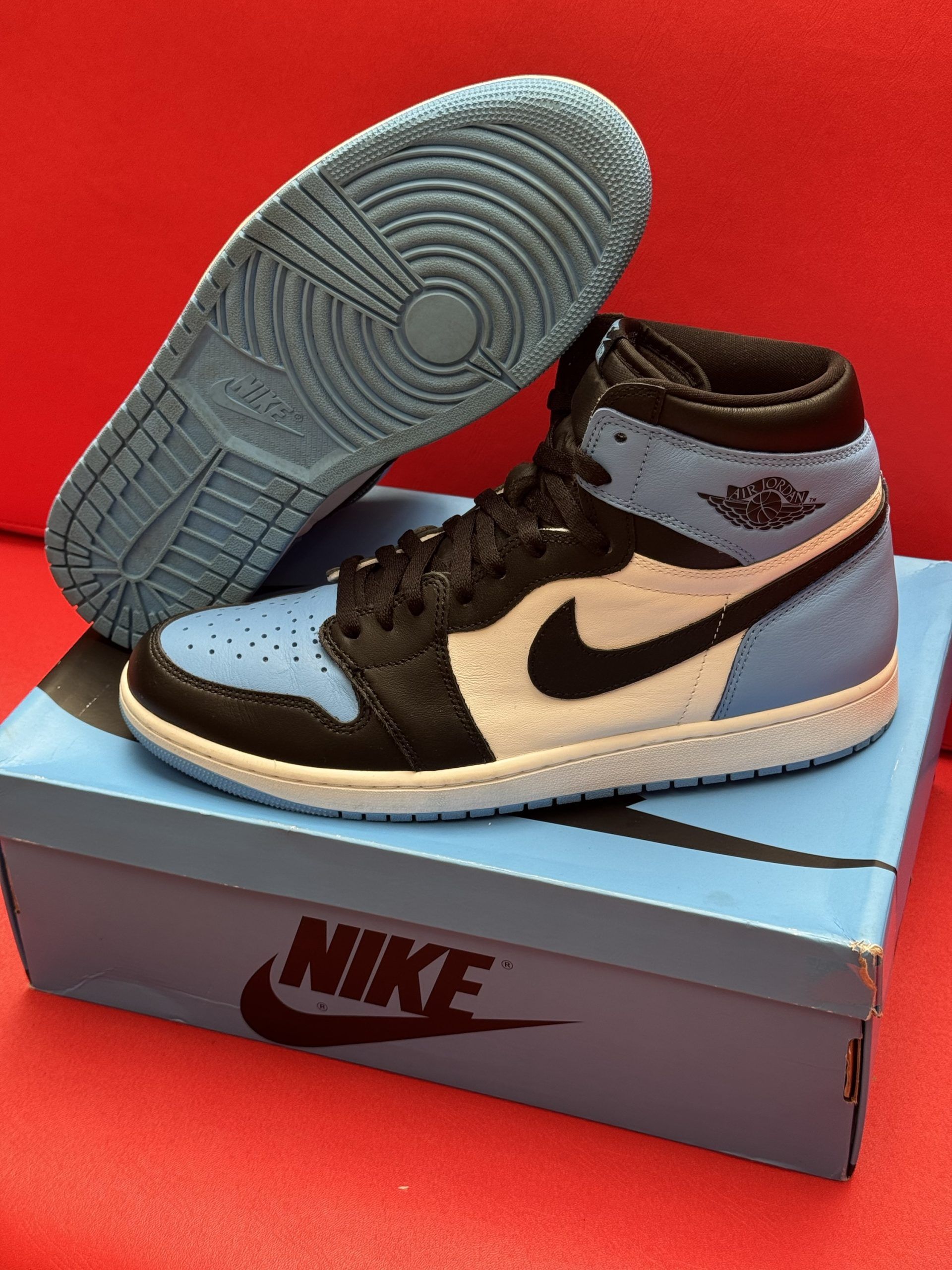 Blue and black Air Jordan 1 sneaker on its box, with a light blue sole visible.