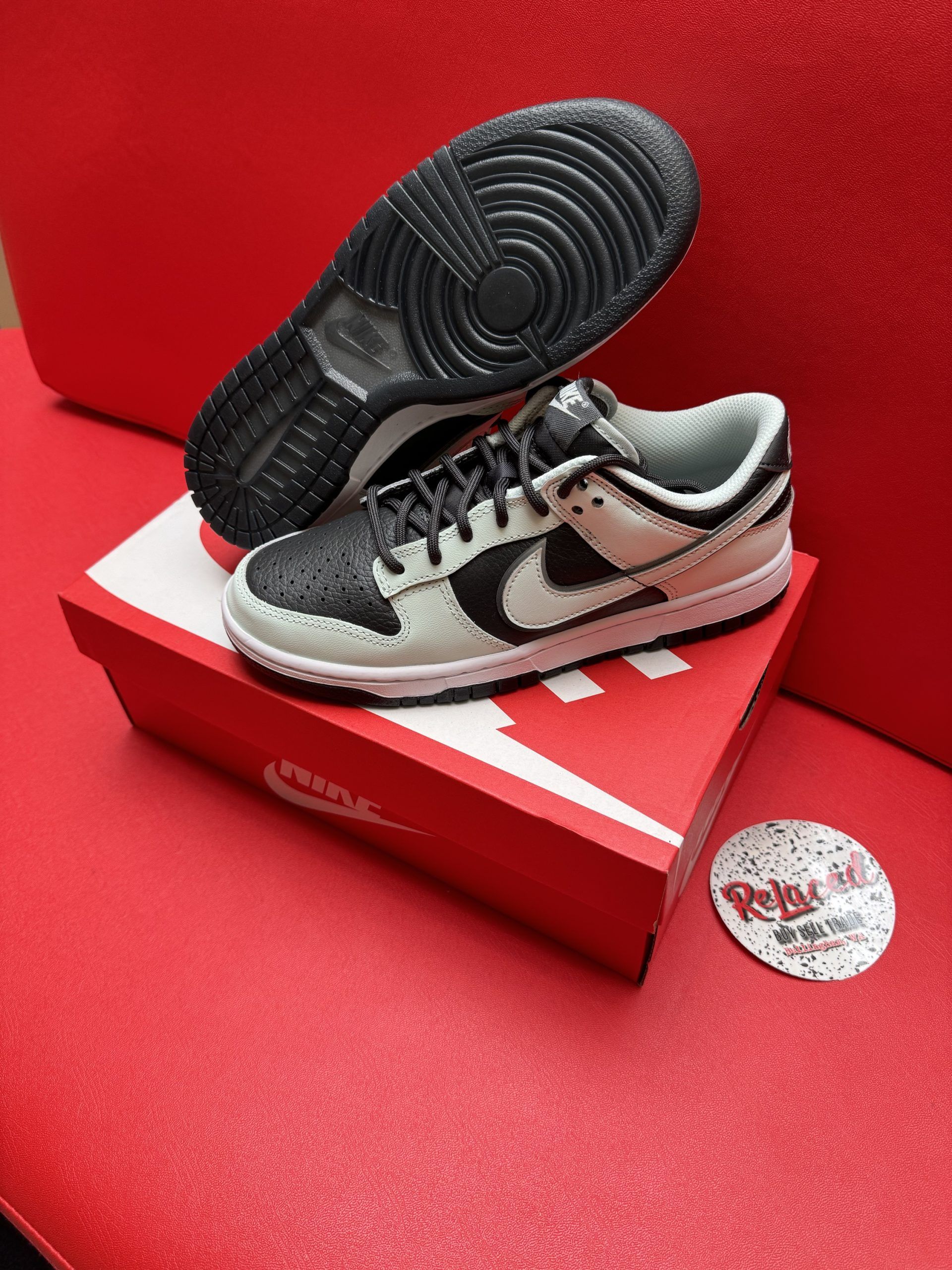 Nike Dunk Low sneakers, black and light gray, on red shoebox, sole visible.