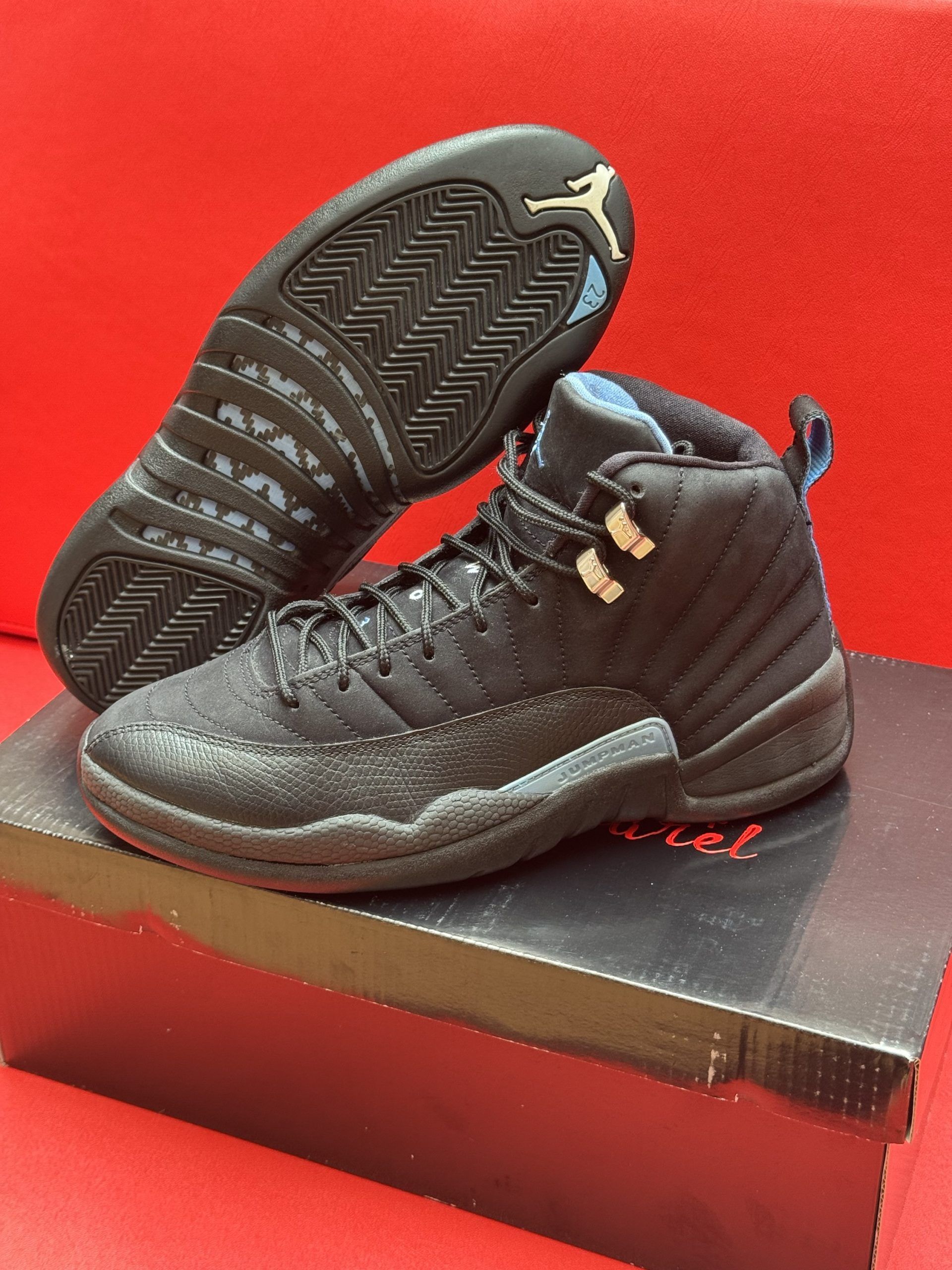 Black and blue Air Jordan 12 sneakers on a black box, displayed against a red background.