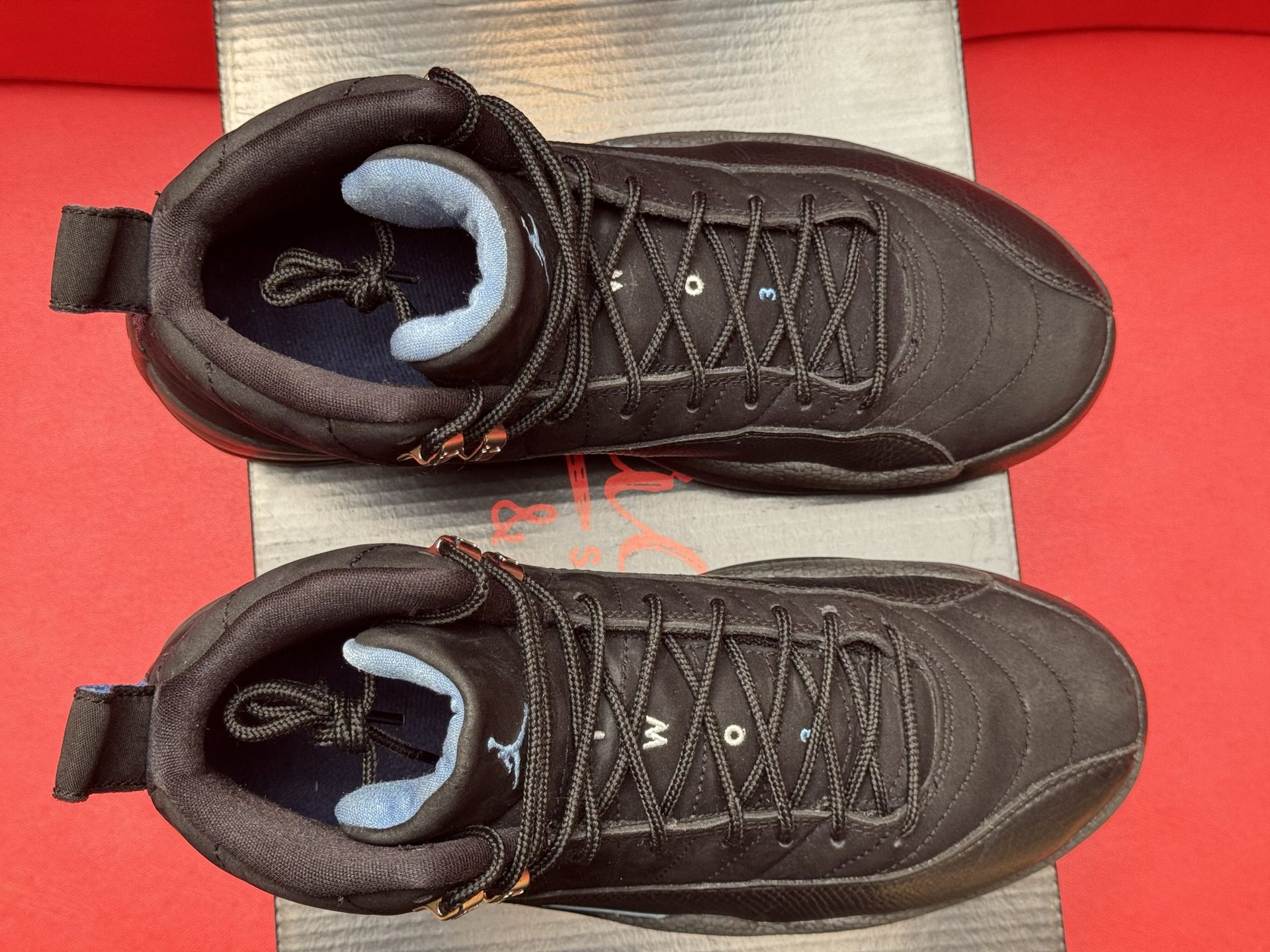 Black and blue Air Jordan 12 sneakers on a black box, displayed against a red background.
