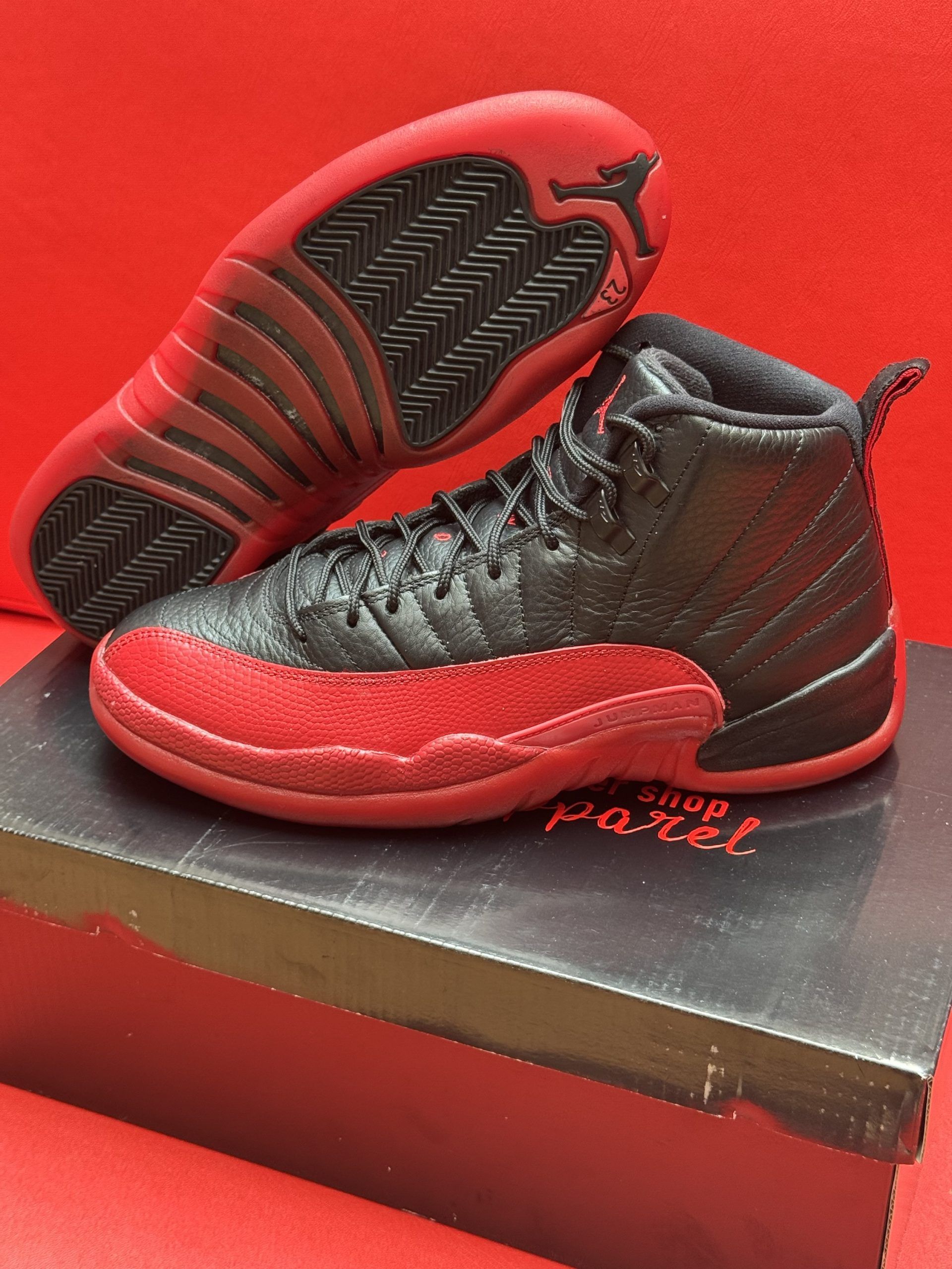 Black and red Air Jordan 12 sneakers on a box. Red sole, black upper.