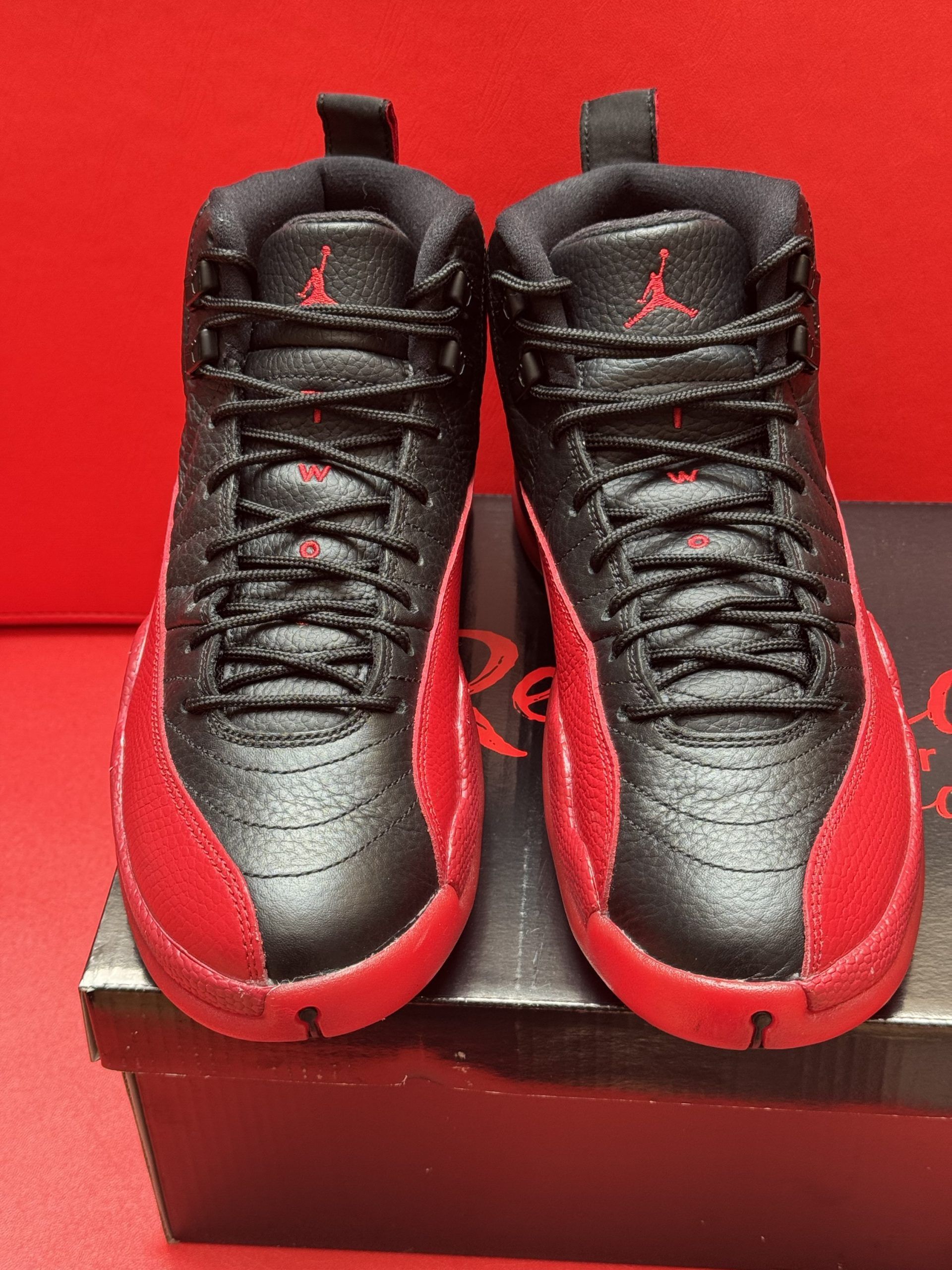 Black and red Air Jordan 12 sneakers on a box. Red sole, black upper.