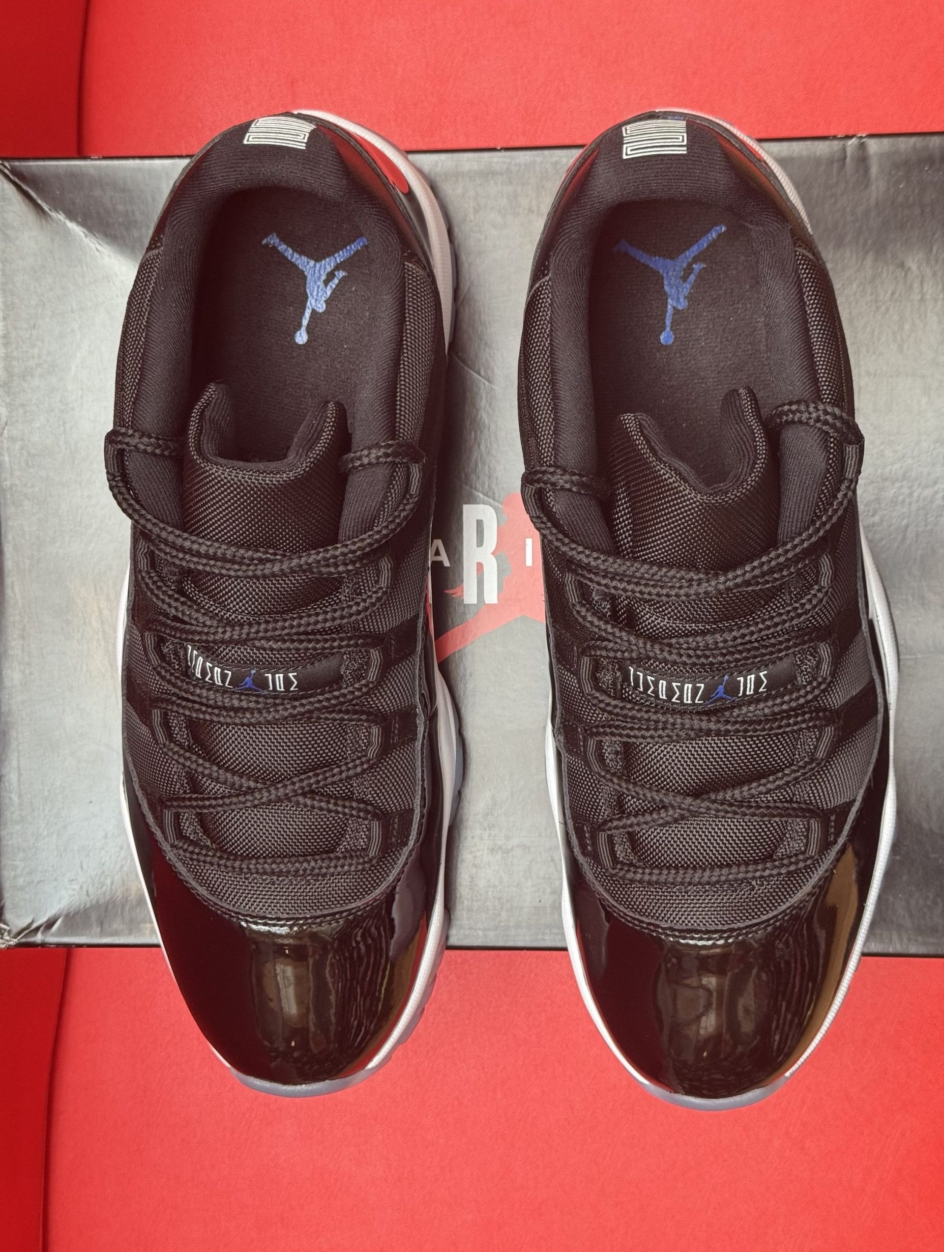 Black and white Air Jordan 11 low-top sneakers on a shoebox, red background.