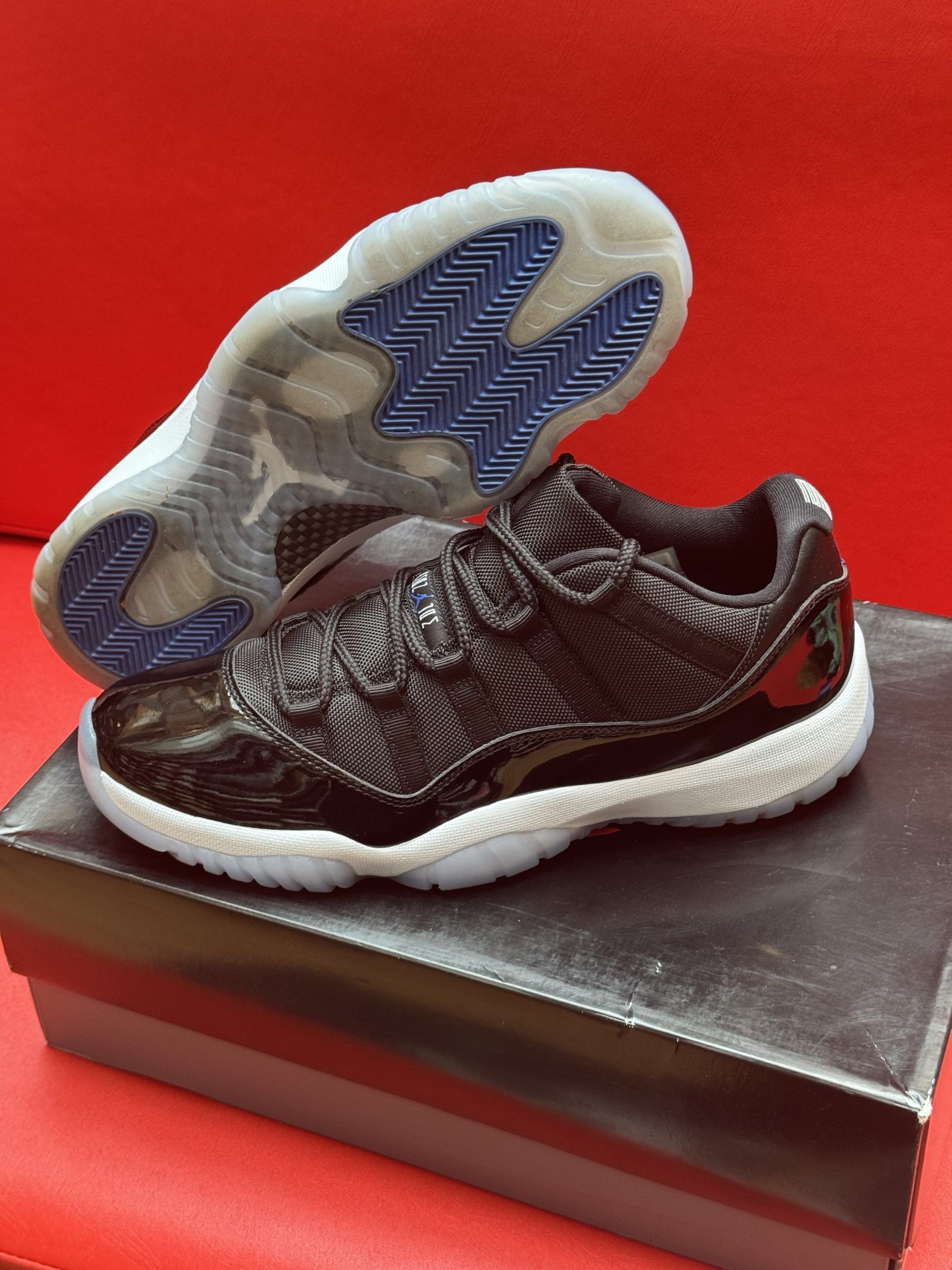 Black and white Air Jordan 11 low-top sneakers on a shoebox, red background.