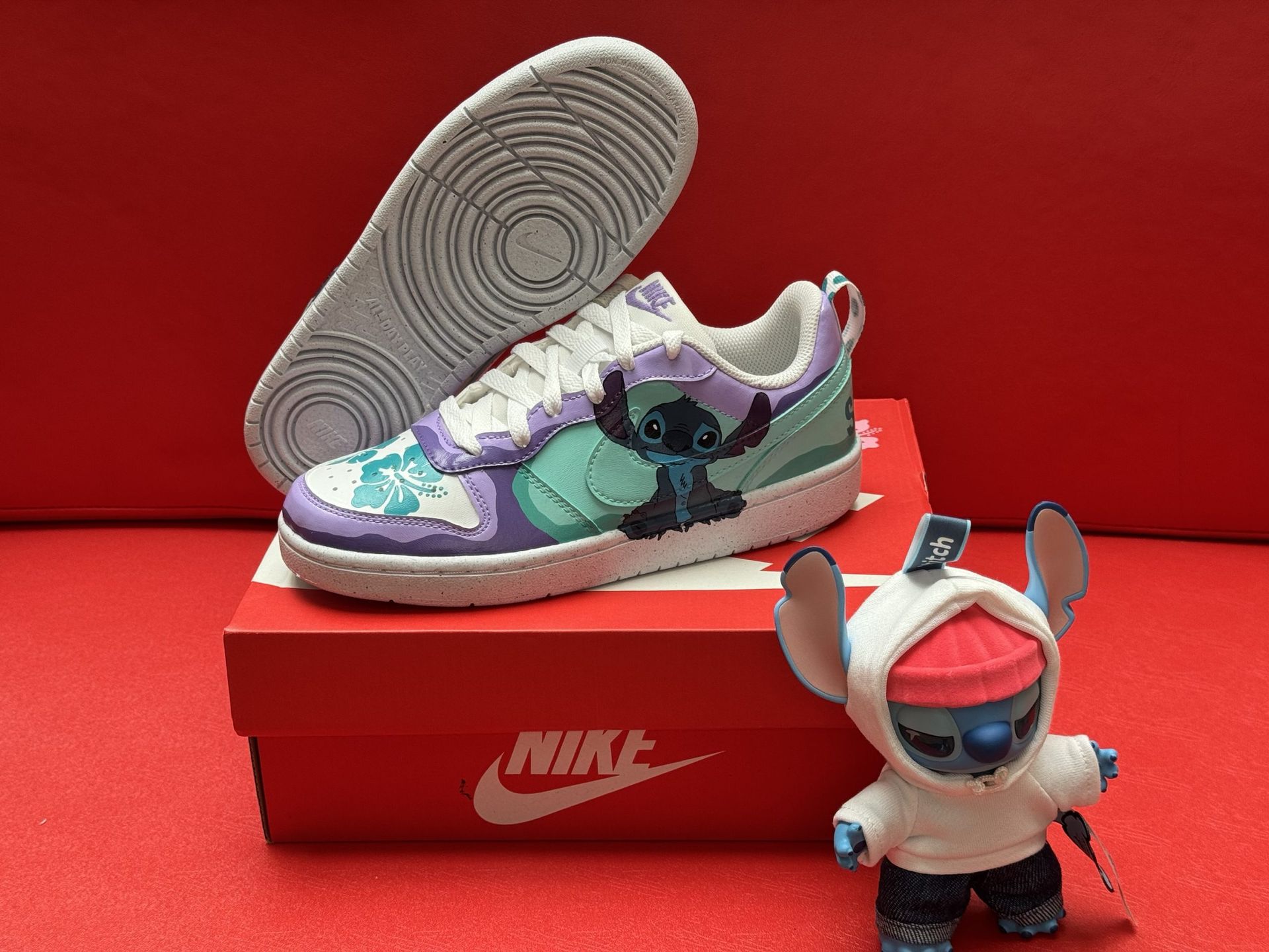 A Nike sneaker featuring Stitch, a blue Disney character, sits on a box, with a figurine of Stitch.