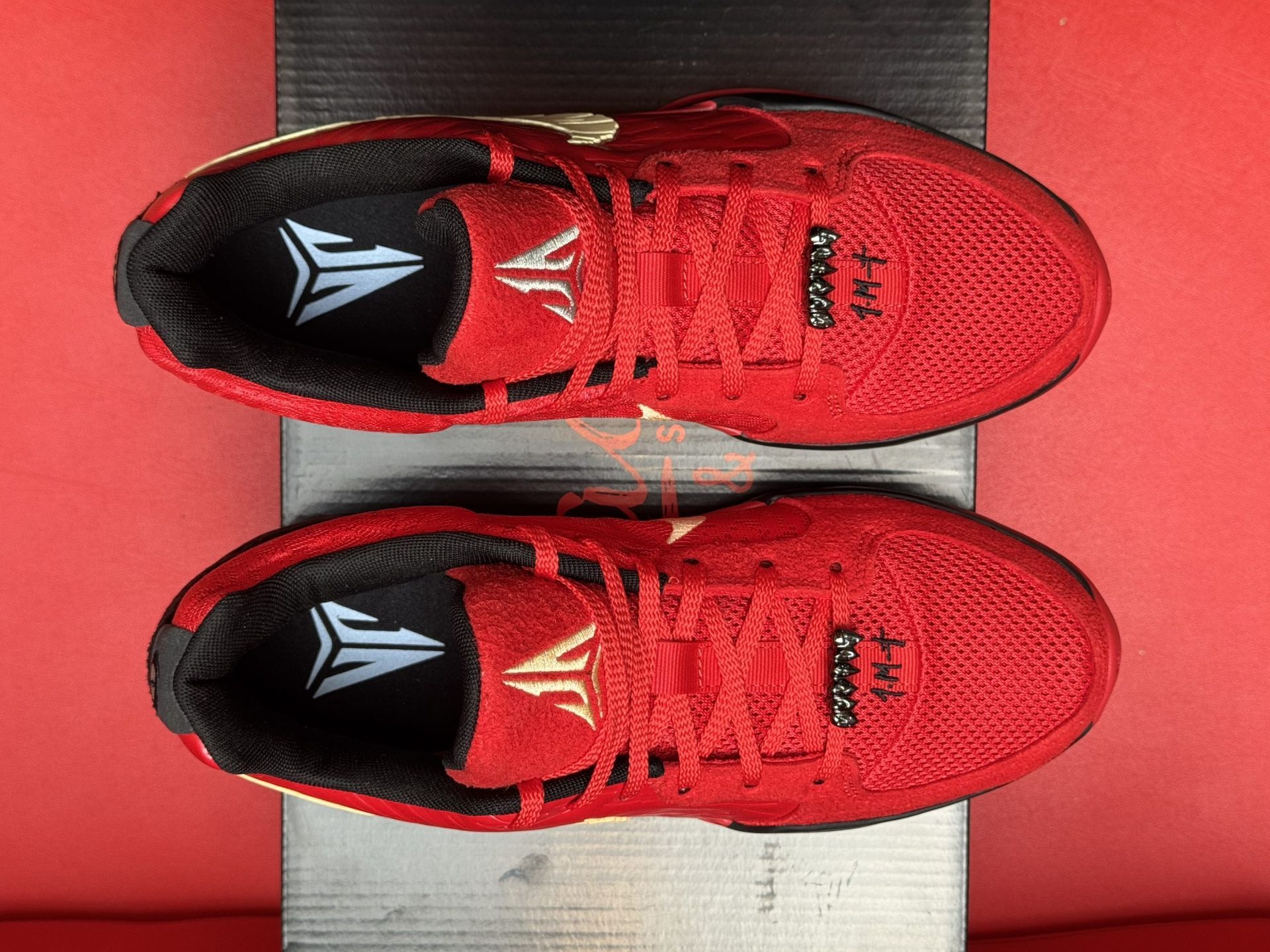 Red Nike basketball sneakers with a gold swoosh on a black box.