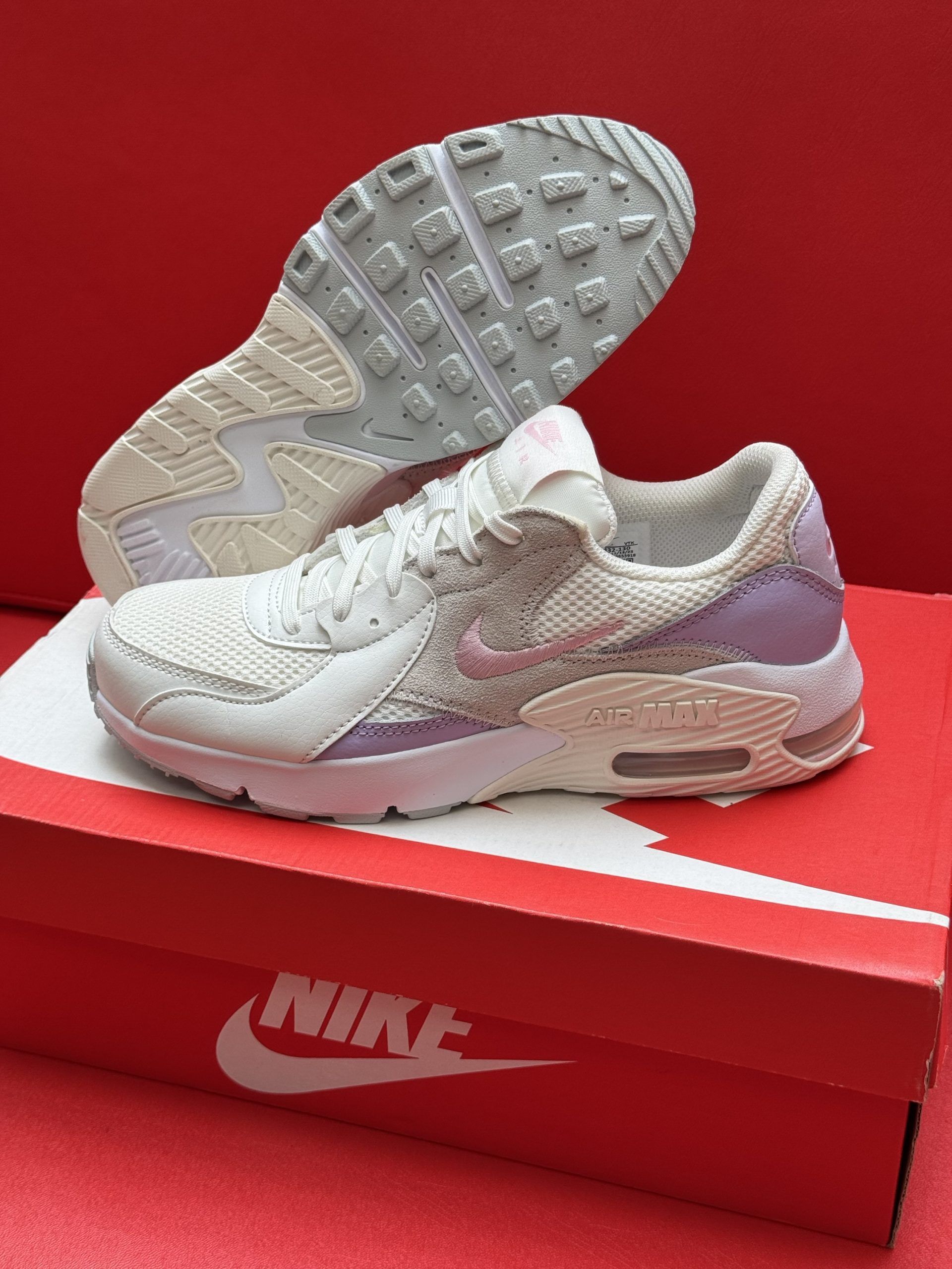 White Nike Air Max Excee sneakers on a red Nike box, showing soles.