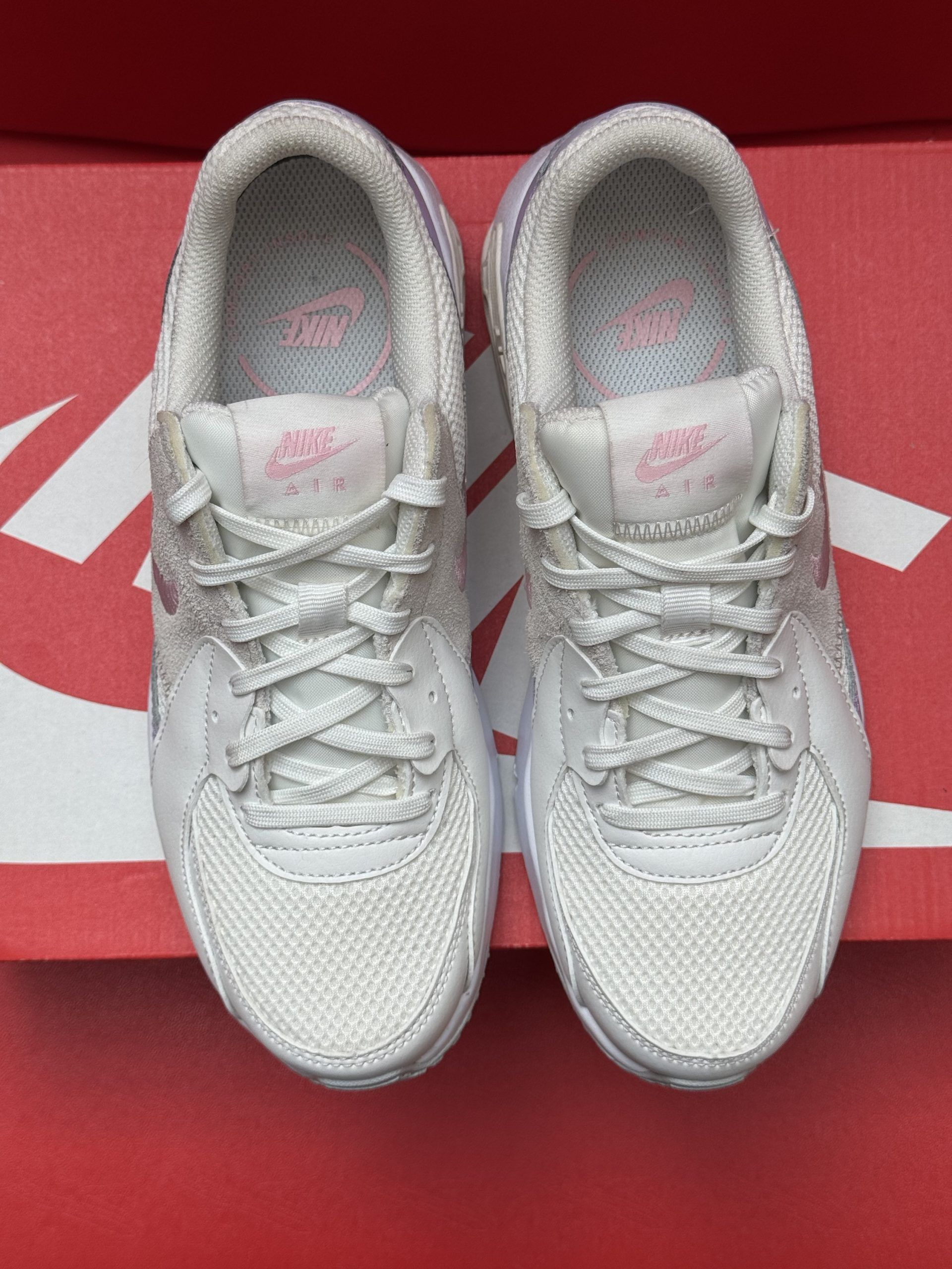 White Nike Air Max Excee sneakers on a red Nike box, showing soles.