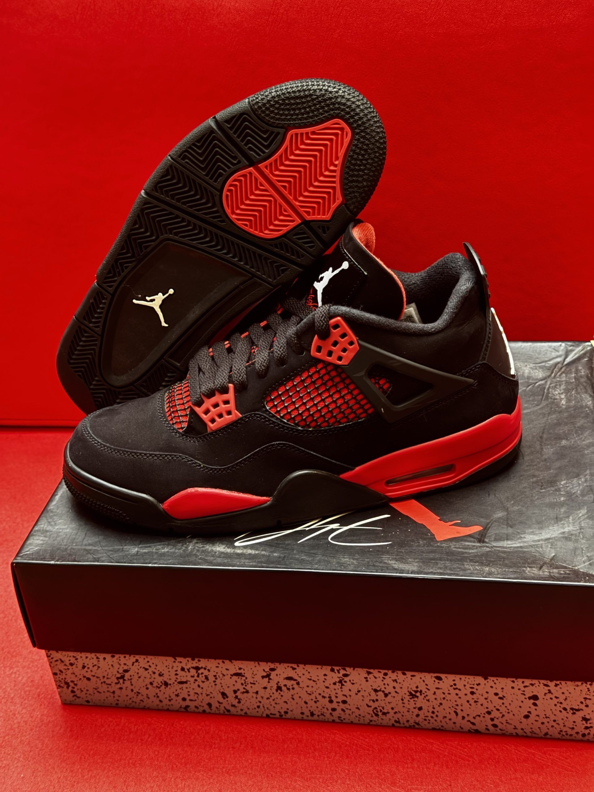 Black and red Air Jordan 4 sneakers on shoebox, red background.