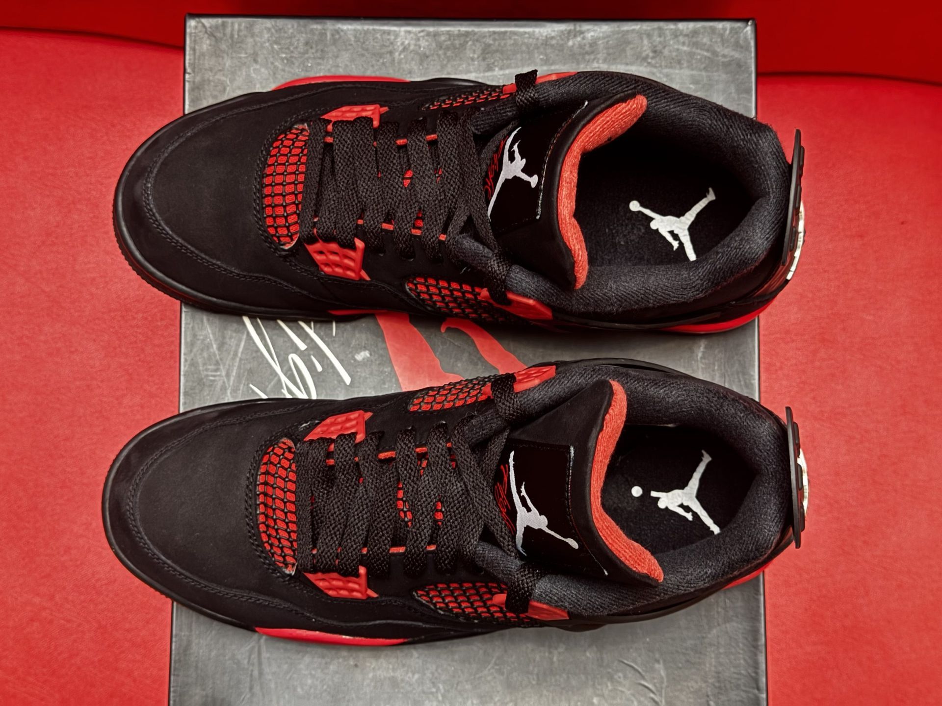 Black and red Air Jordan 4 sneakers on shoebox, red background.