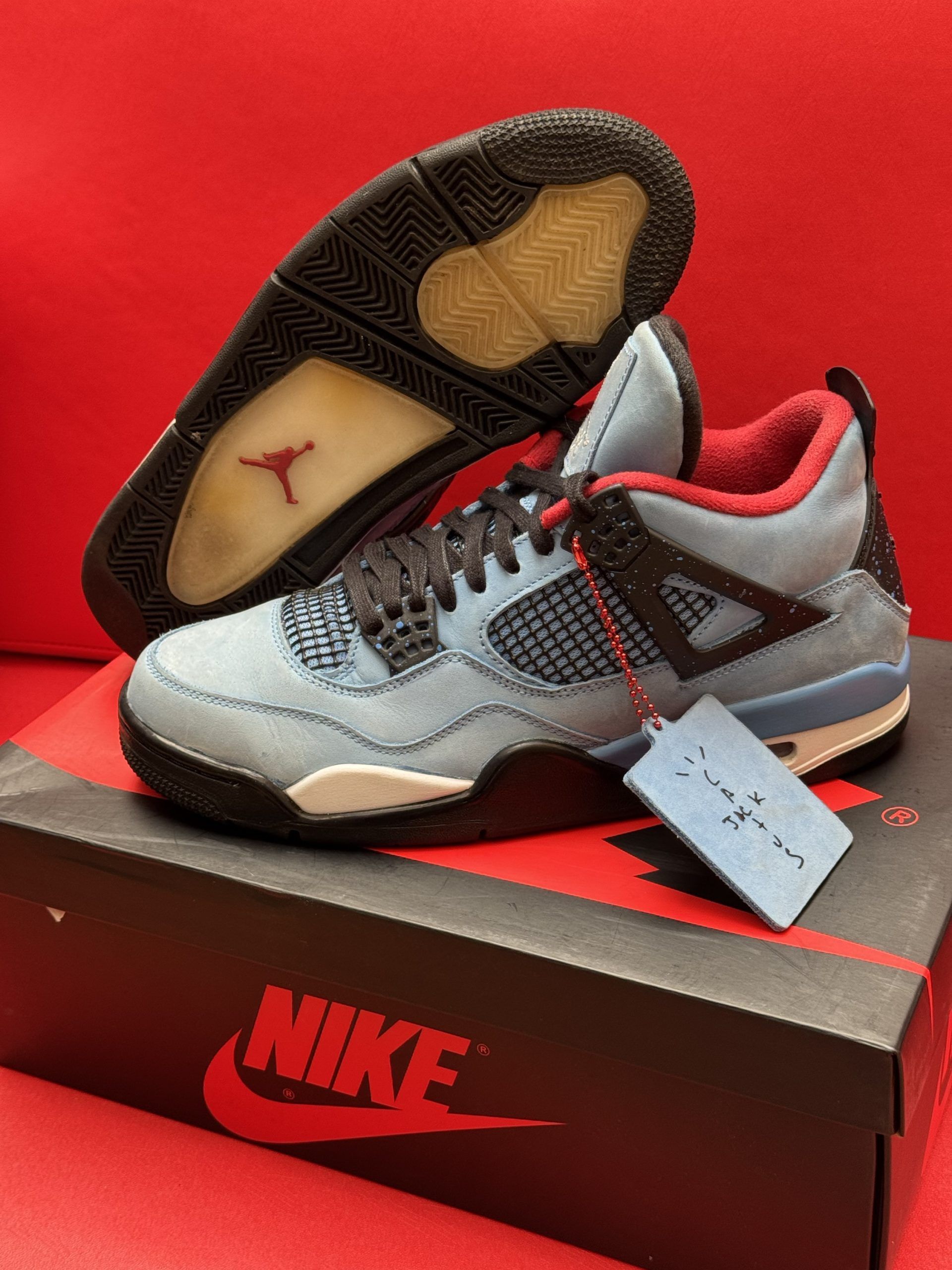 Blue, red, and brown Air Jordan 4 sneakers on top of a black Nike shoe box with a red background.