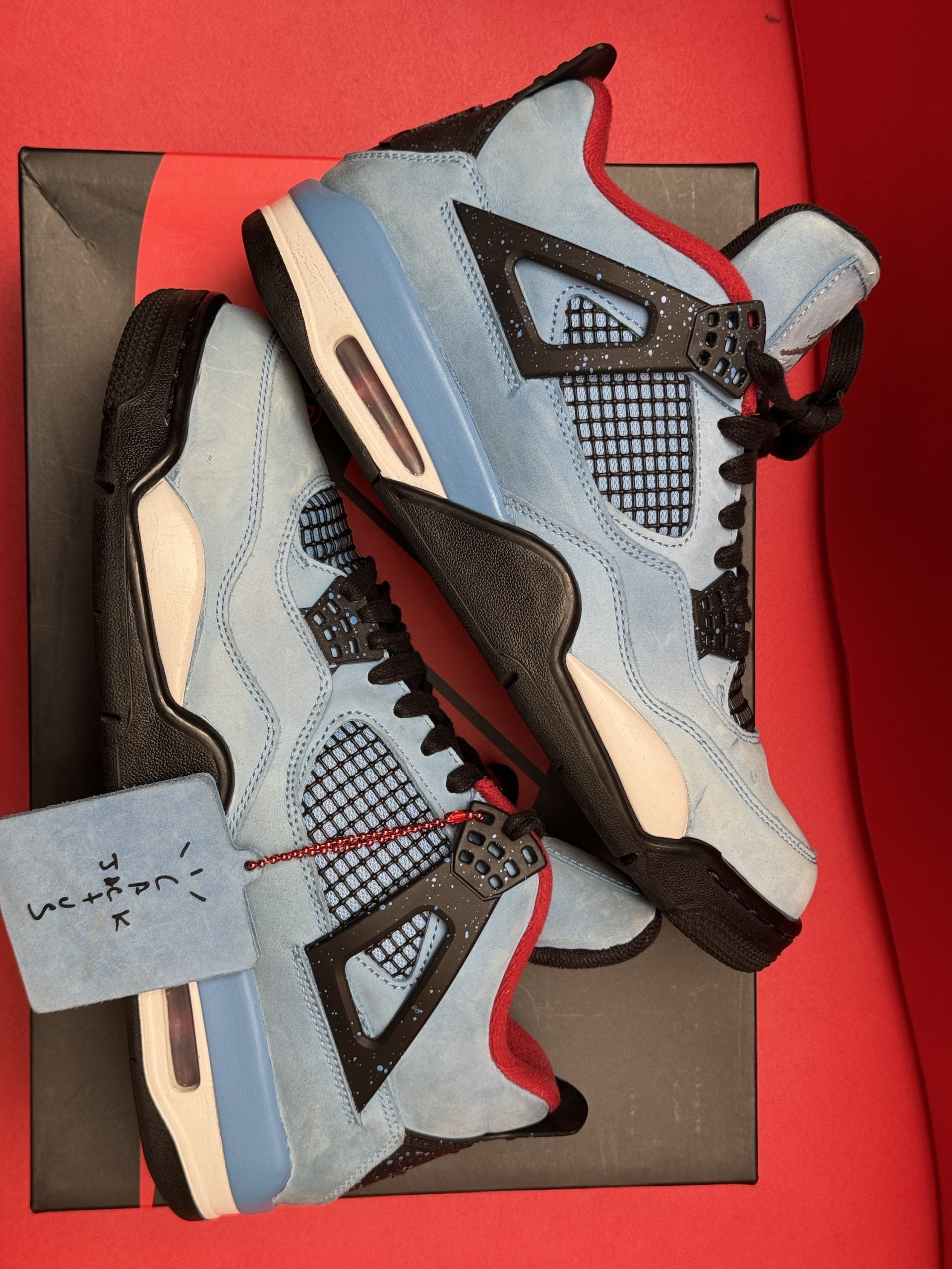 Blue, red, and brown Air Jordan 4 sneakers on top of a black Nike shoe box with a red background.