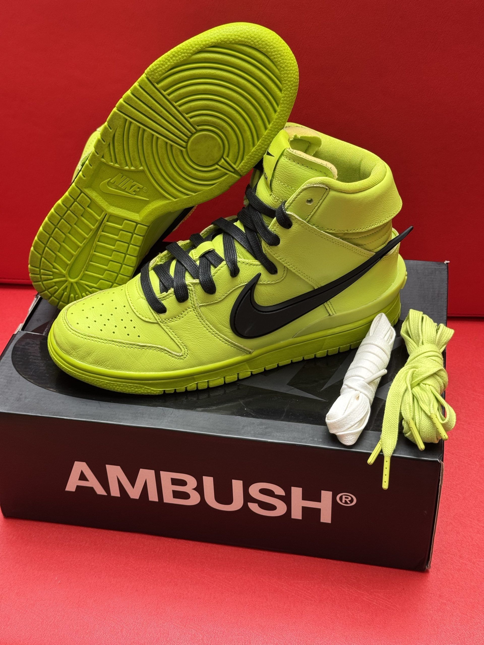 Green Nike high-top sneakers with black laces, a black swoosh, and a neon green sole, sitting on an AMBUSH shoe box.