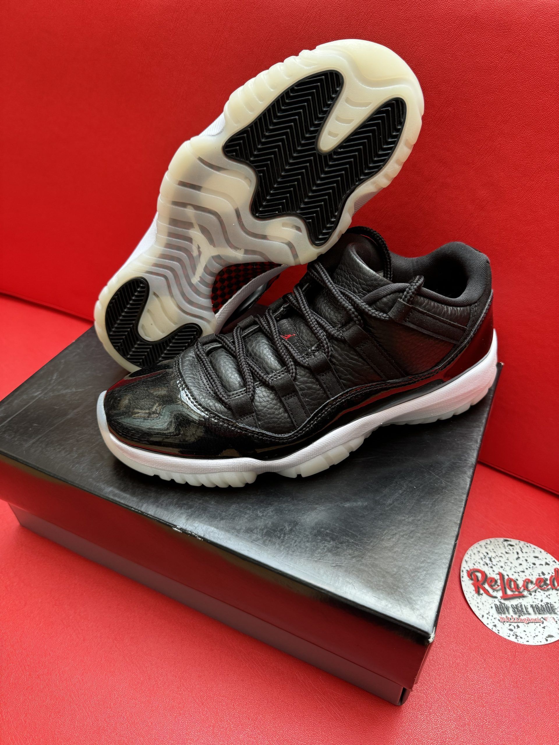 Black and white toddler sneakers with shiny material, white sole, and black laces, on a black box, against a red background.