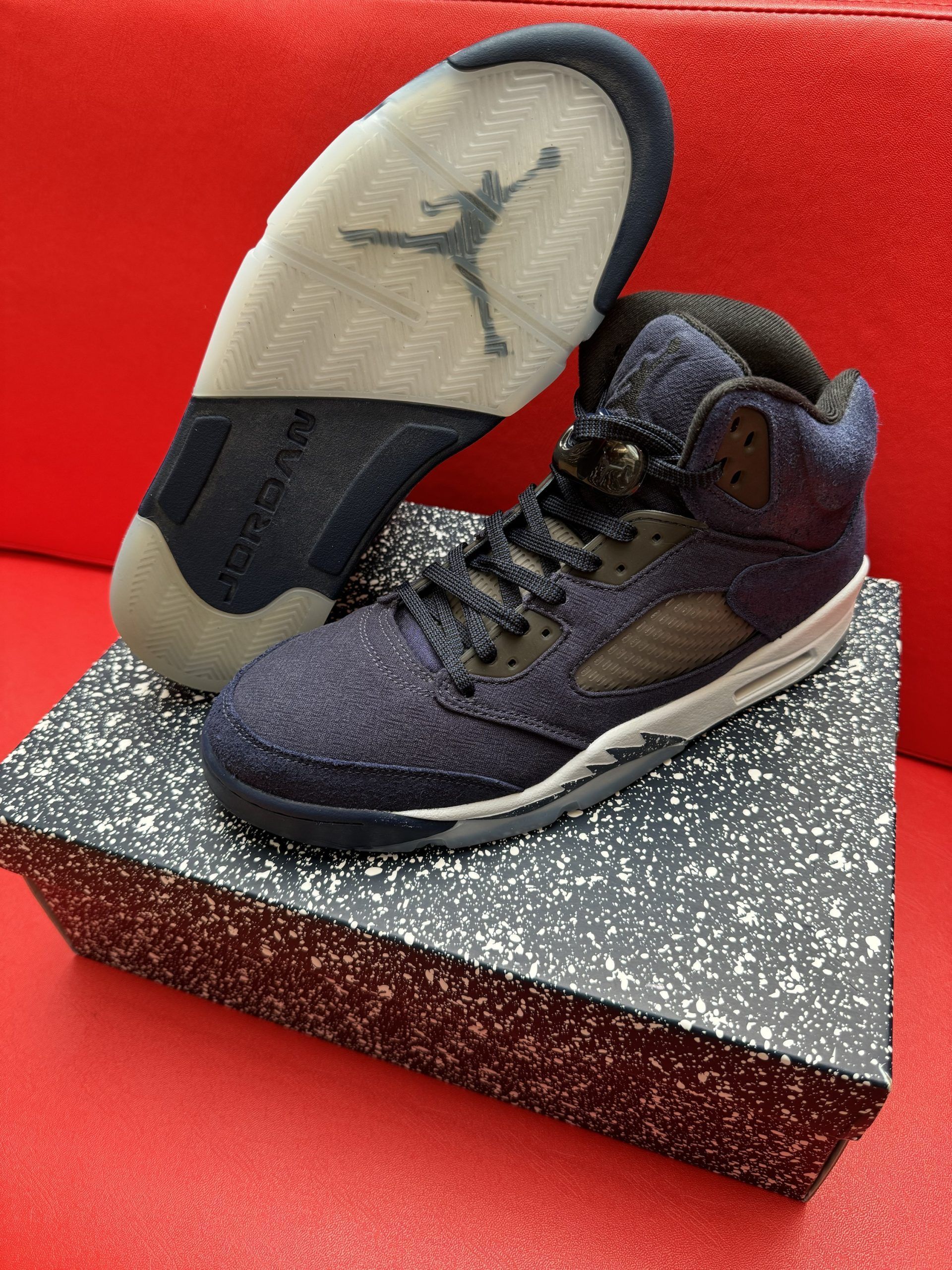 Blue and gray Air Jordan 5 sneakers on a speckled box, showing the sole with the Jumpman logo.