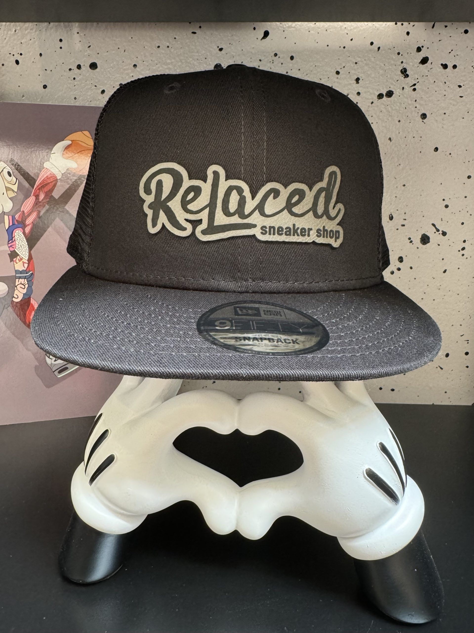 Black hat with "Relaced Sneaker Shop" logo on a Mickey Mouse hand display.