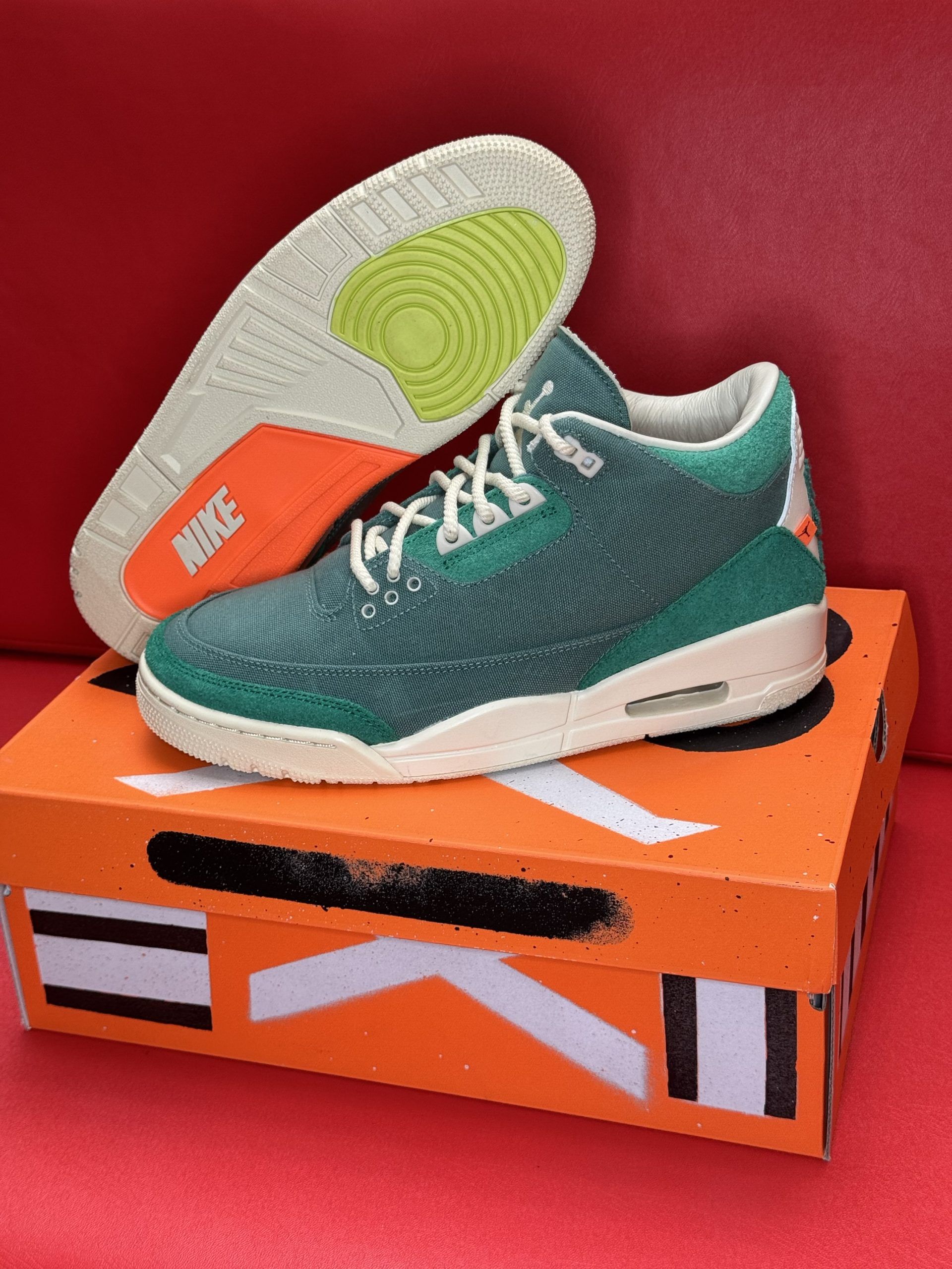 Green and cream Air Jordan sneakers on an orange shoebox, one sole up.