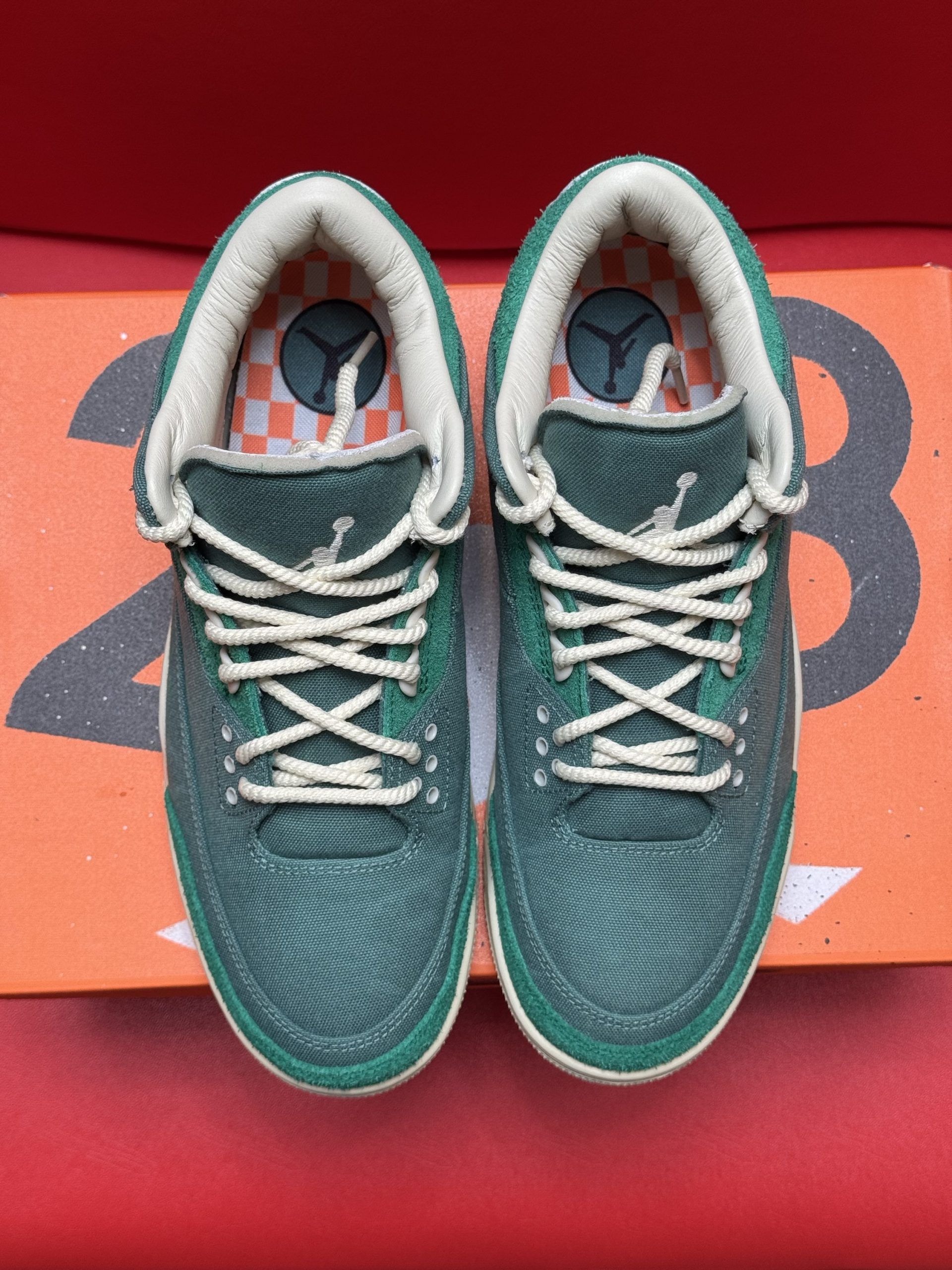Green and cream Air Jordan sneakers on an orange shoebox, one sole up.