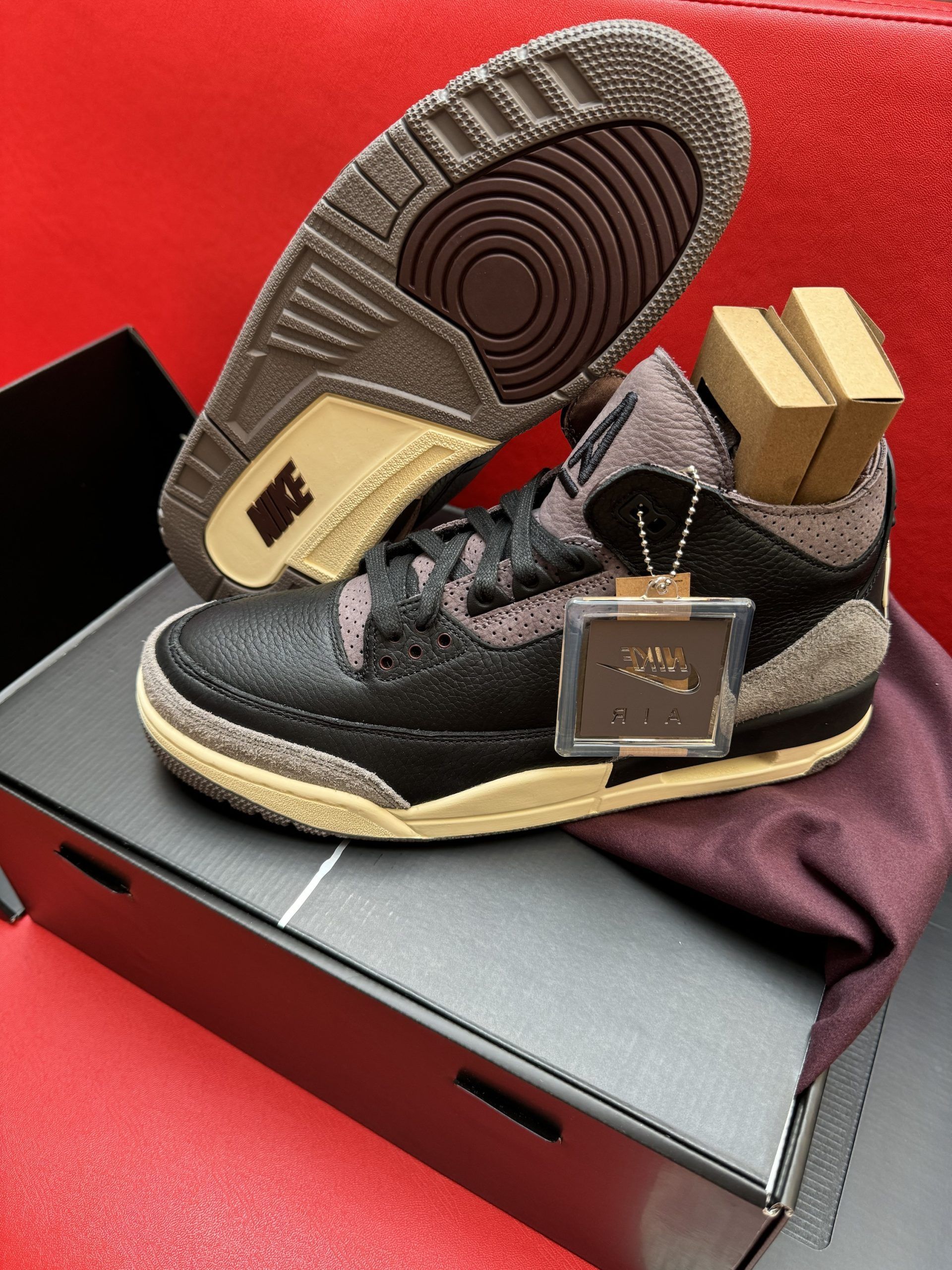 A pair of black and brown Air Jordan 3 sneakers with a brown sole, tag, and small boxes inside.