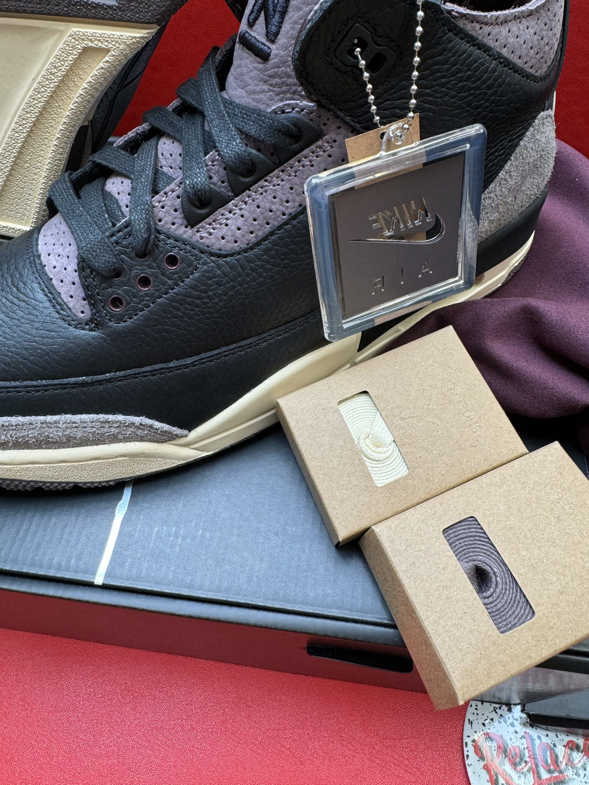 A pair of black and brown Air Jordan 3 sneakers with a brown sole, tag, and small boxes inside.