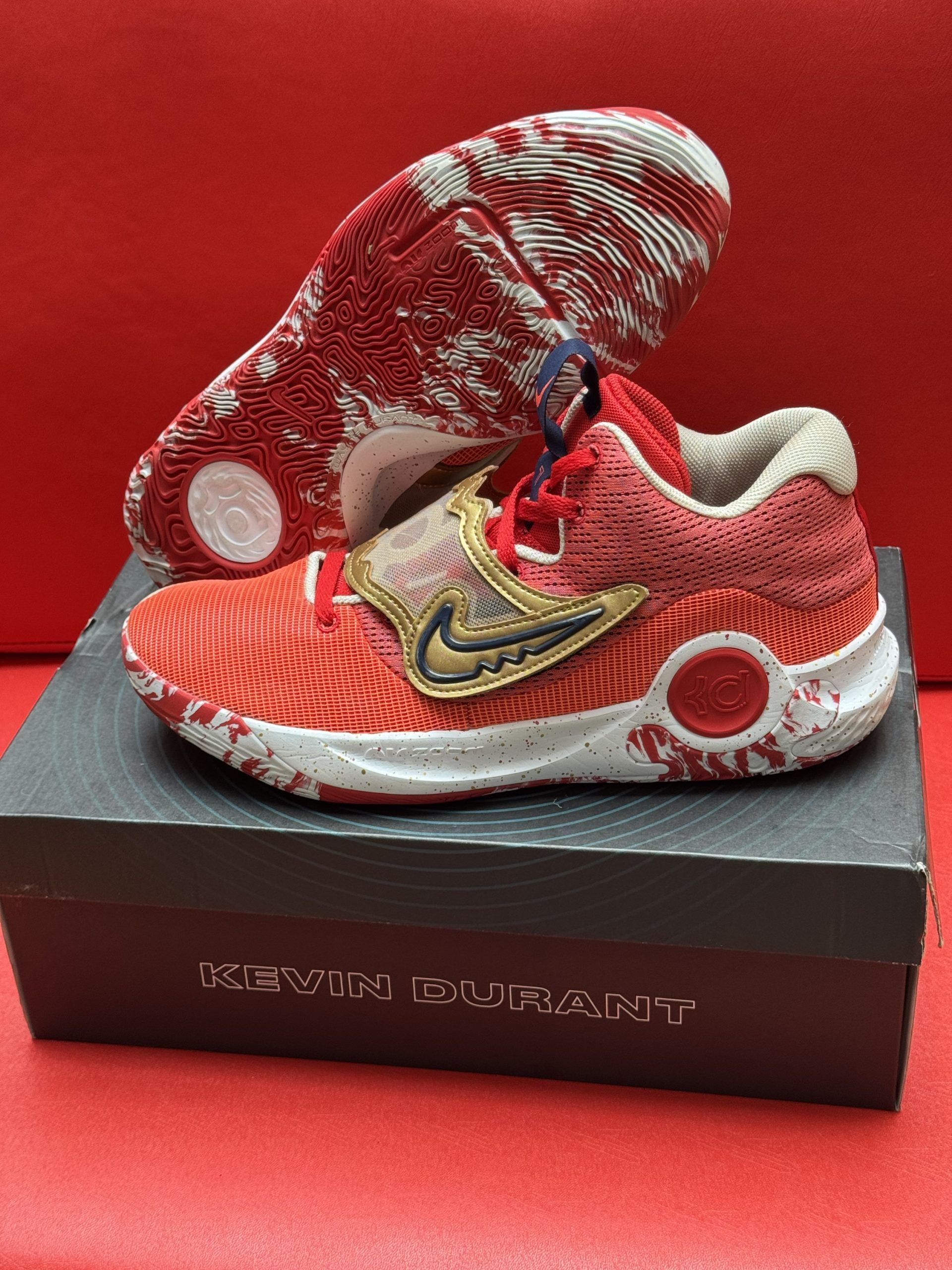Red and gold Nike KD basketball shoes with white accents, sitting on a box that says 