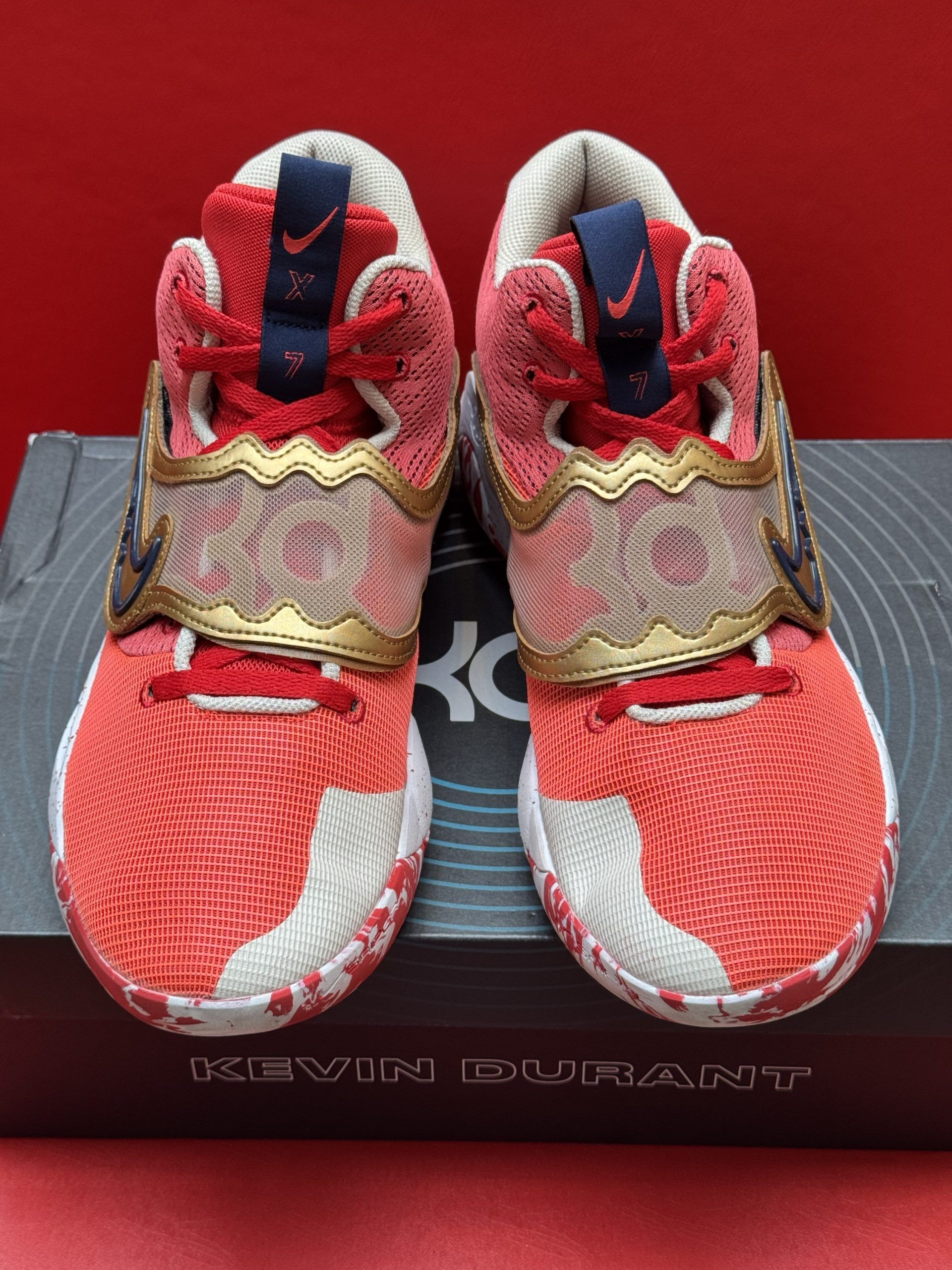 Red and gold Nike KD basketball shoes with white accents, sitting on a box that says 