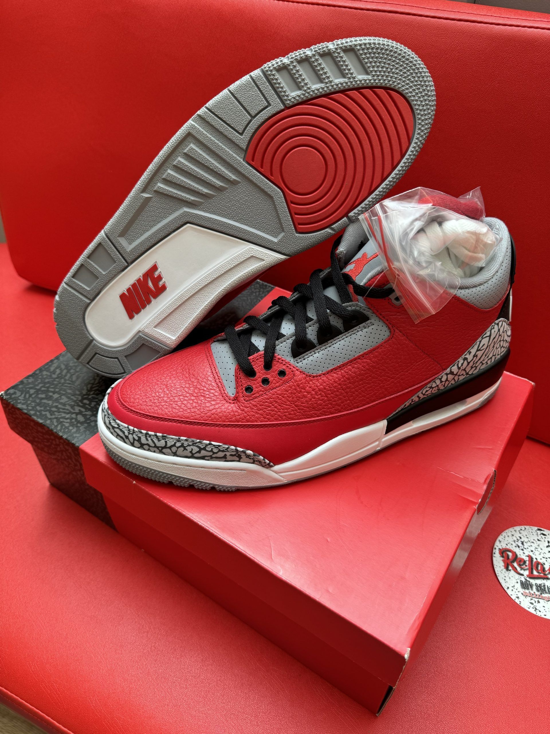 Red and gray Air Jordan 3 sneakers with black laces on a red box.